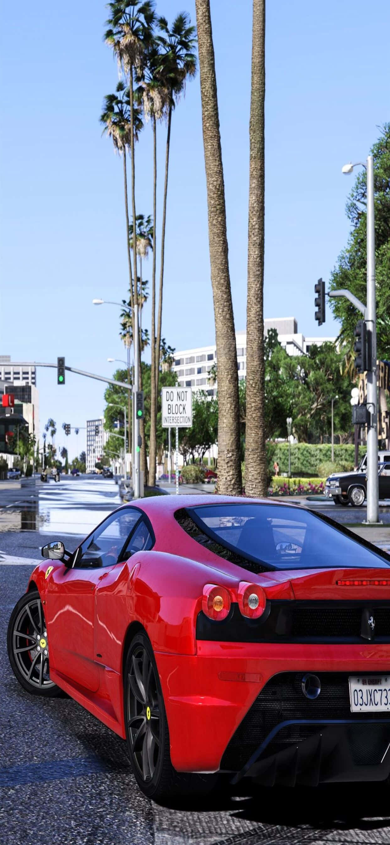 iPhone XS Max《GTA V》紅色克爾維特背景 壁紙 — 一輛充滿活力的紅色法拉利跑車停泊在陽光普照、棕櫚樹成蔭的城市街道上，背景有交通燈和現代建築。