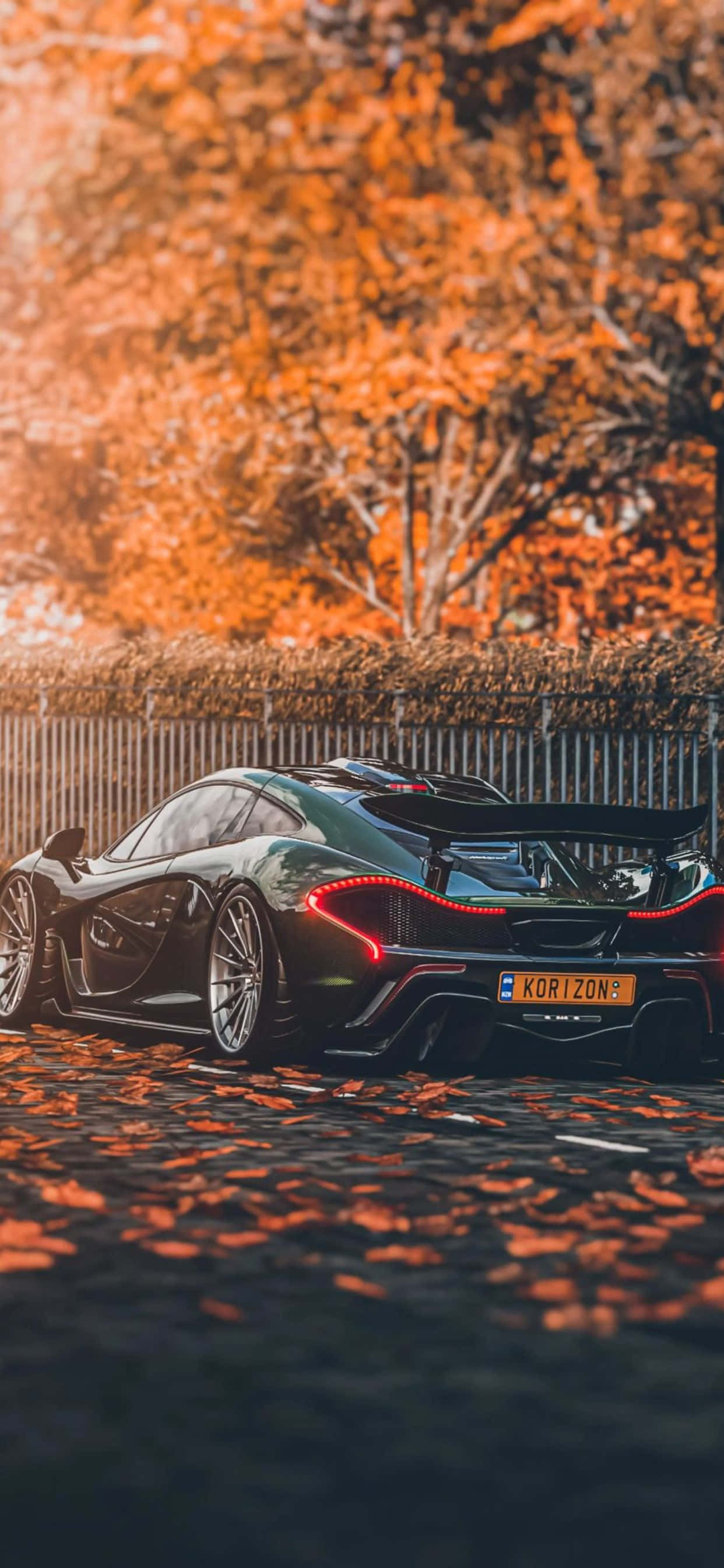 風格與力量的完美結合 — iPhone XS Max 與 McLaren 720S 壁紙 — 一輛時尚的黑色跑車，帶有發光的紅色尾燈，停在落葉覆蓋的鵝卵石街道上，周圍是秋樹。