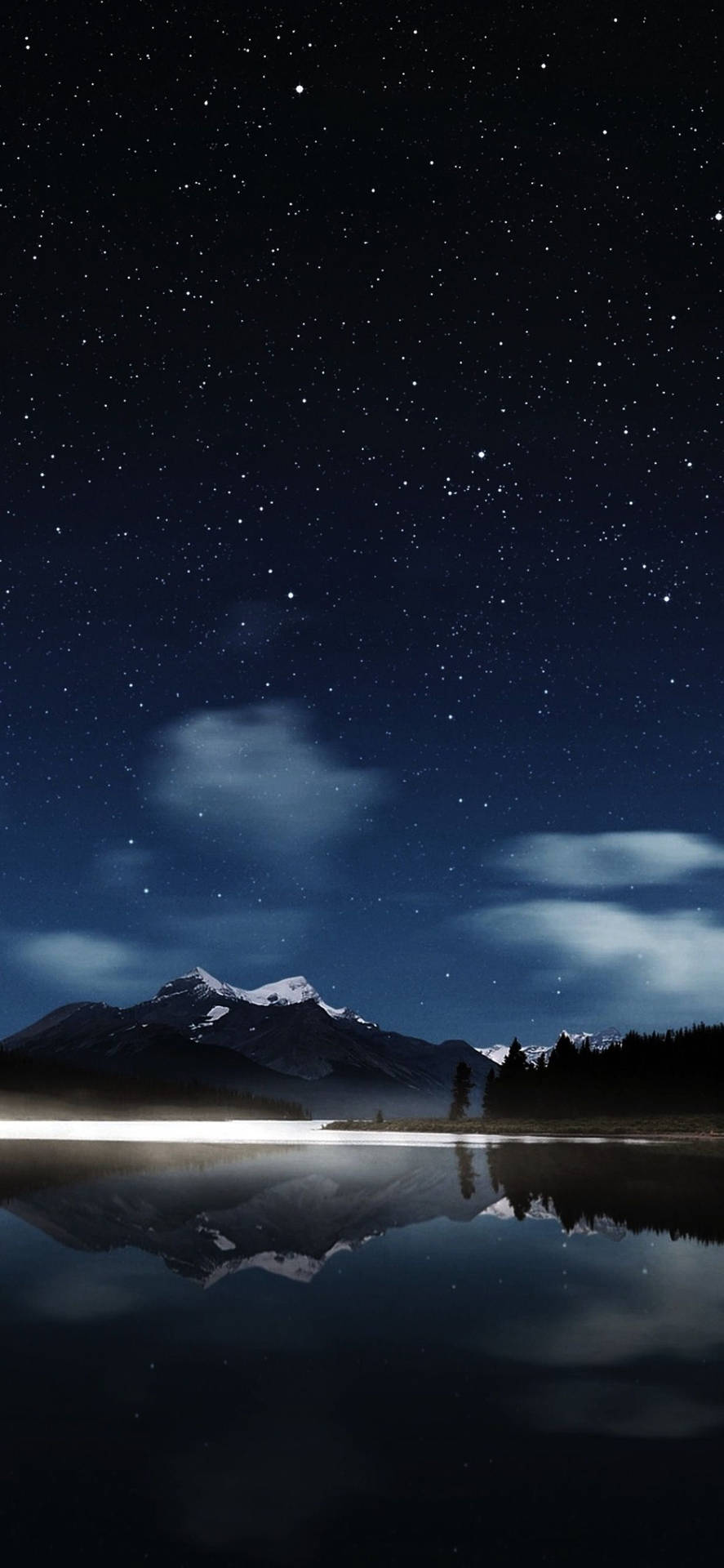 星空夜空倒映在平靜的湖面上，伴有積雪的山峰和樹木。