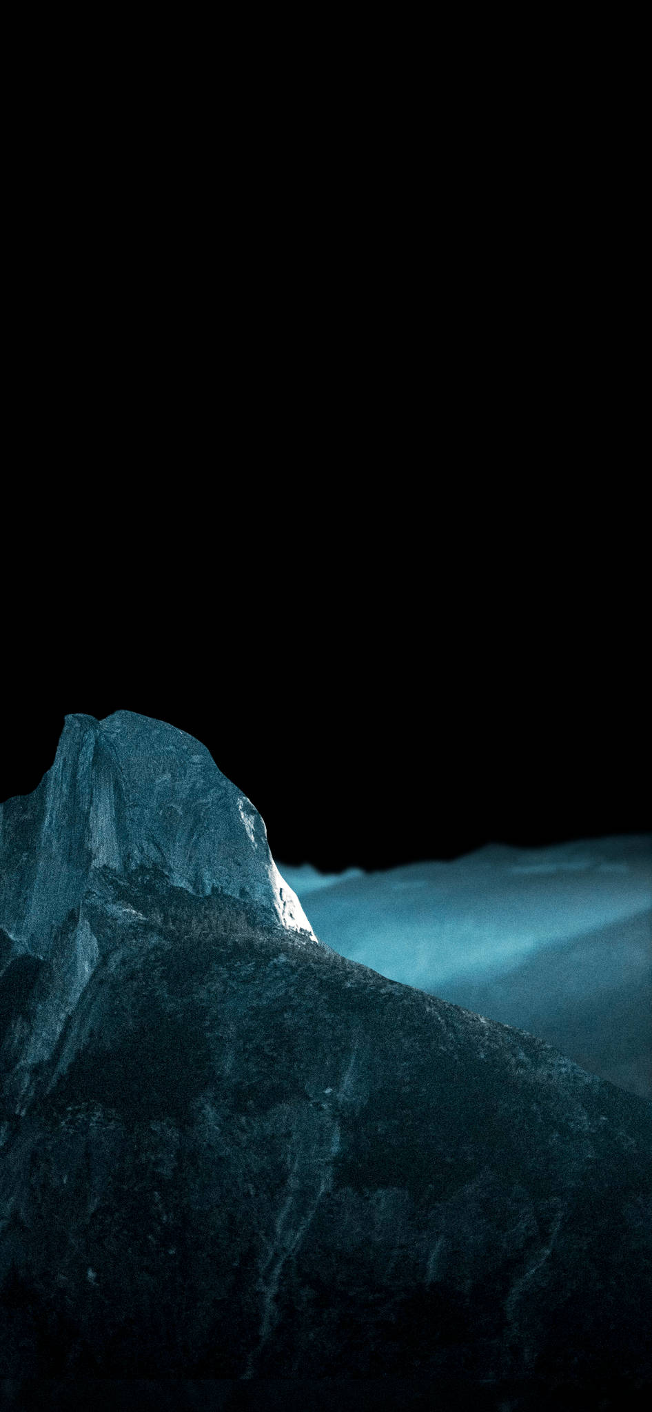 iPhone XS Max OLED 藍色山脈 壁紙 — 孤獨的山峰在漆黑的天空和霧氣瀰漫的山谷之上散發出冷藍色的光芒。