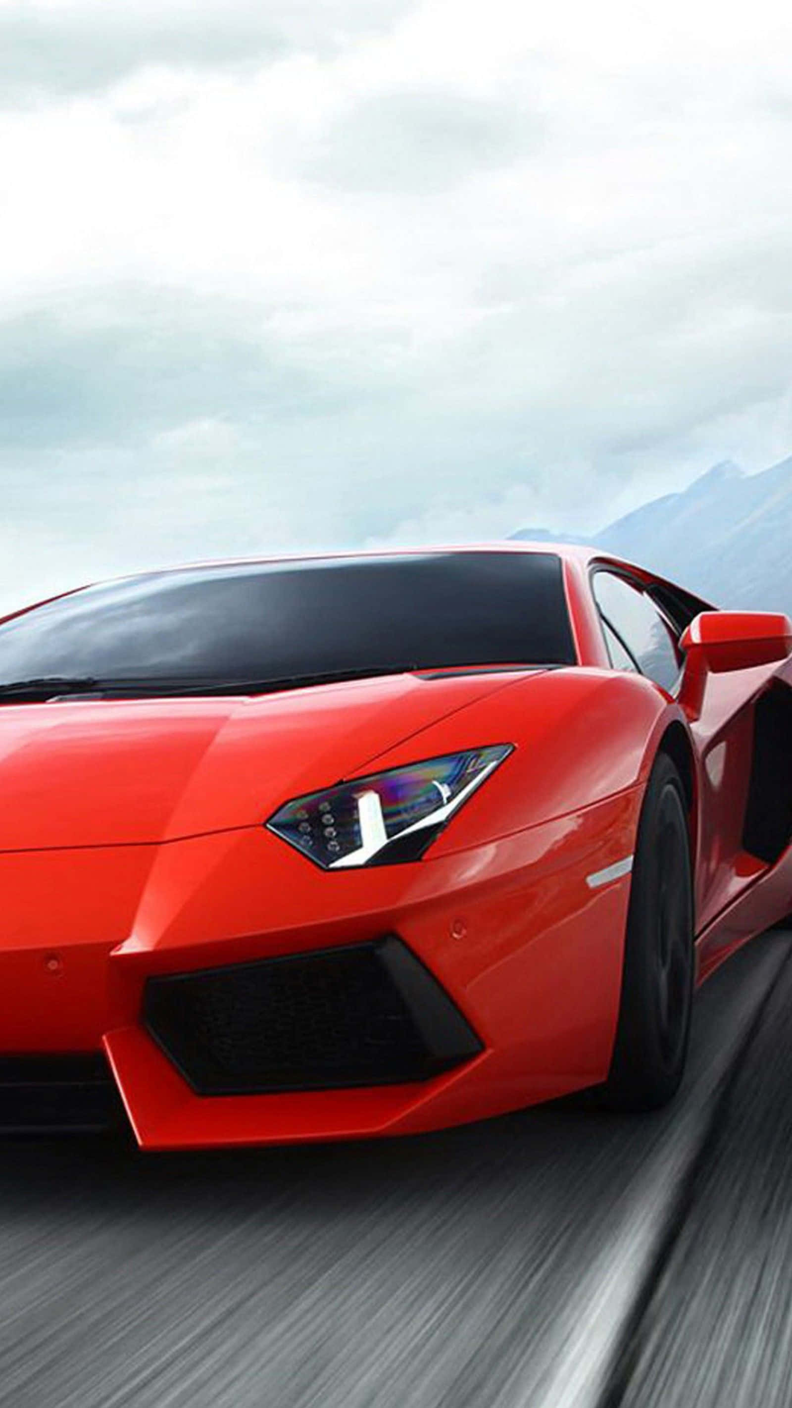 iPhone XS Max《Project CARS 2》紅色 2012 愛馬仕 Aventador 背景 壁紙 — 一輛鮮紅色的跑車在陰天天空下沿著山路疾馳，帶有模糊的動態效果。