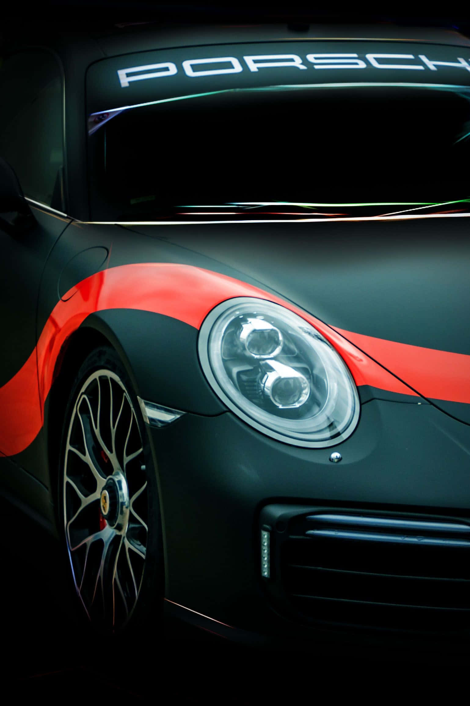 iPhone XS Max《Project CARS 2》黑底紅色保時捷 911 背景 壁紙 — 一輛時尚的黑色保時捷跑車，帶有醒目的紅色賽車條紋，在戲劇性的工作室燈光下閃耀。