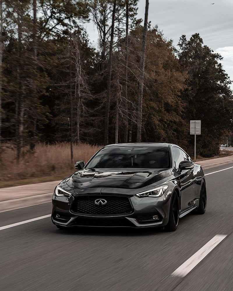 iPhone XS Max Project Cars 2 黑色英菲尼迪 Q60 背景 壁紙 — 一輛時尚的黑色 Infiniti 跑車在陰天下行駛在森林環繞的道路上。
