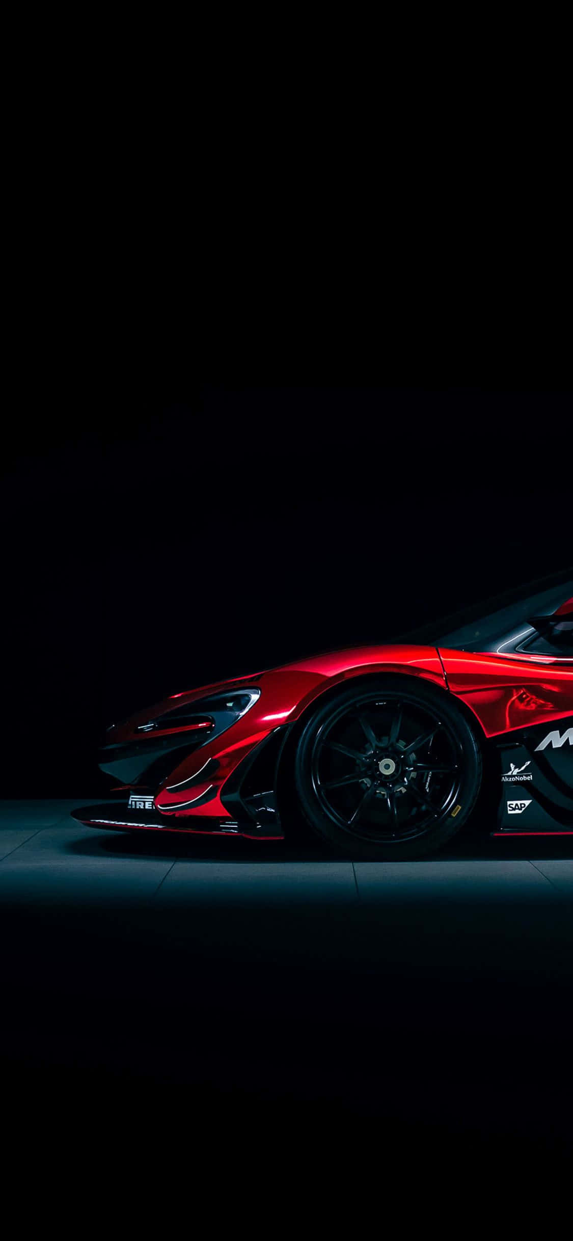 iPhone XS Max《Project Cars 2》紅色麥拉倫P1 GTR背景 壁紙 — 一輛流線型紅色跑車在戲劇性聚光燈下，以漆黑工作室背景襯托，閃閃發光。