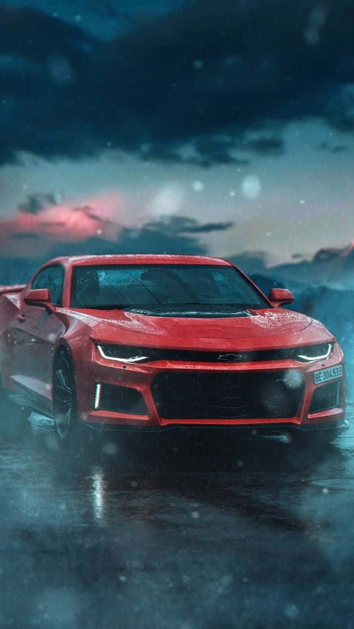 iPhone XS Max《Project Cars 2》紅色雪佛蘭科邁羅背景 壁紙 — 一輛紅色跑車在潮濕的道路上，在帶有粉紅色和藍色雲朵的陰沉暮色天空下，閃爍著雨滴的光芒。