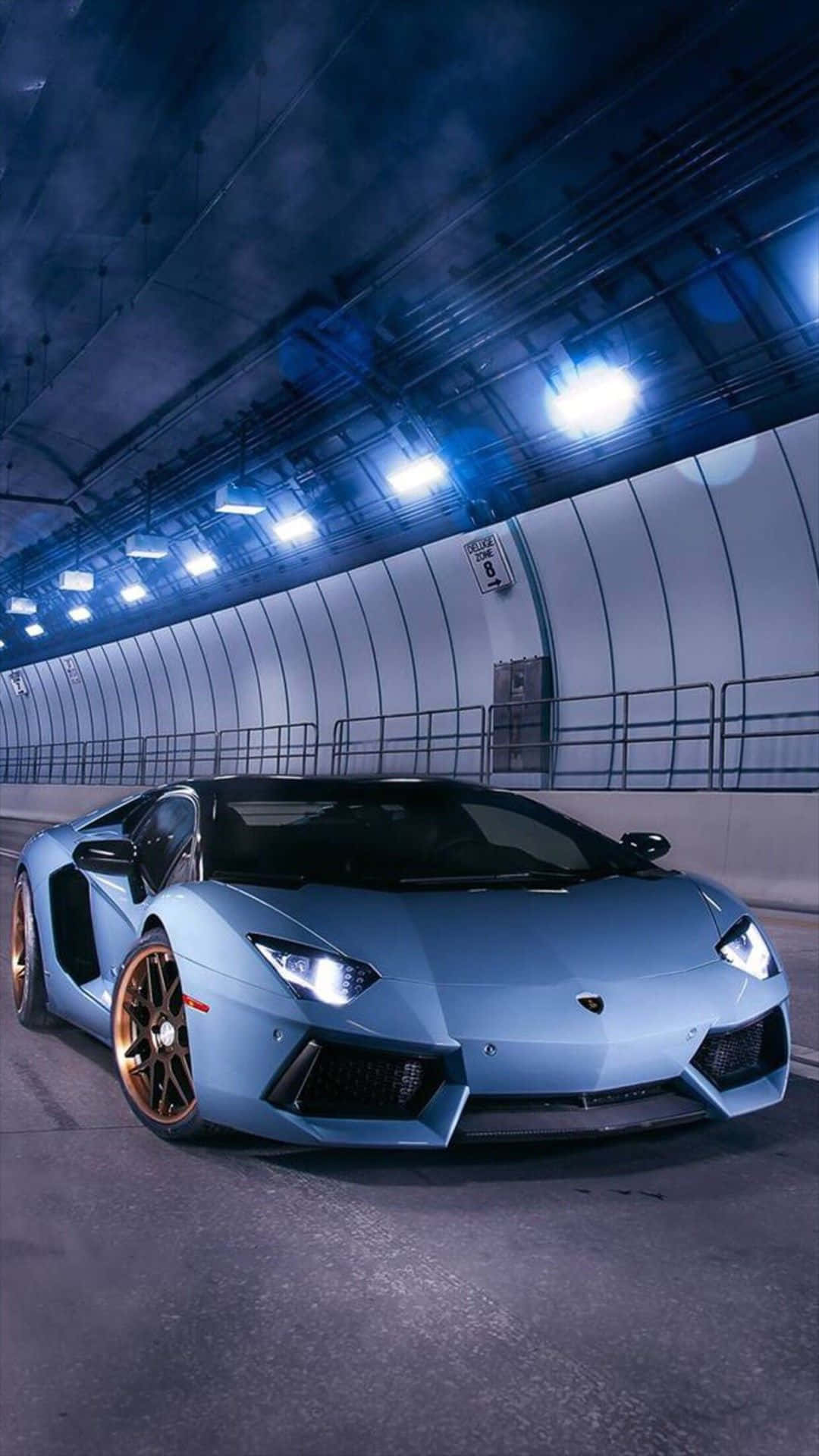 iPhone XS Max《Project CARS 2》淺藍色愛馬仕 Aventador 背景 壁紙 — 一輛時尚的淺藍色林寶堅尼 Aventador 配金色輪圈，在頭頂藍色燈光照亮的昏暗隧道中滑行。