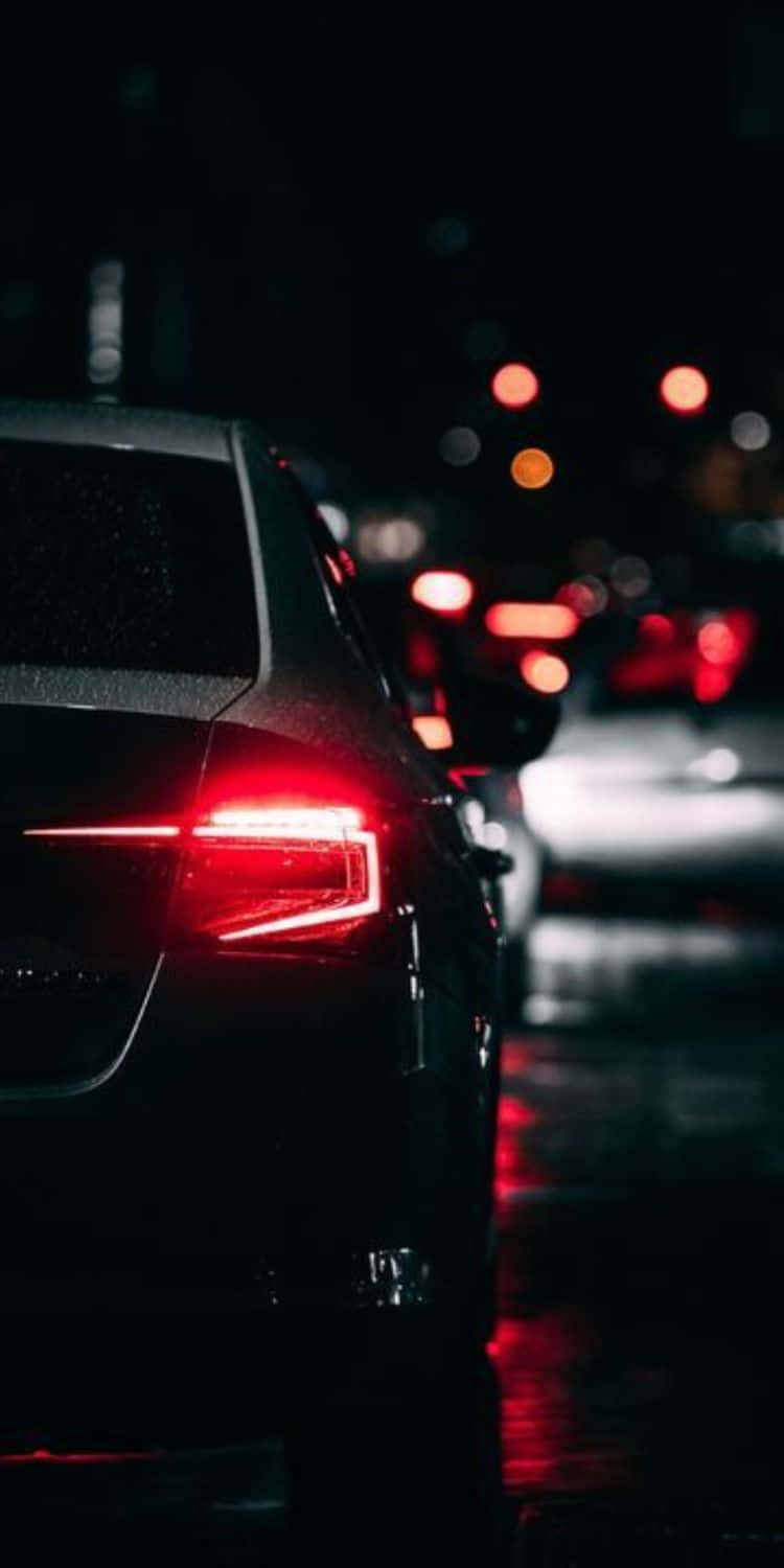 在 iPhone XS Max 上享受《Project CARS 2》的刺激賽車體驗 壁紙 — 一輛時尚汽車的紅色尾燈在黑暗夜空下映照在濕漉漉的路面上，城市燈光模糊。