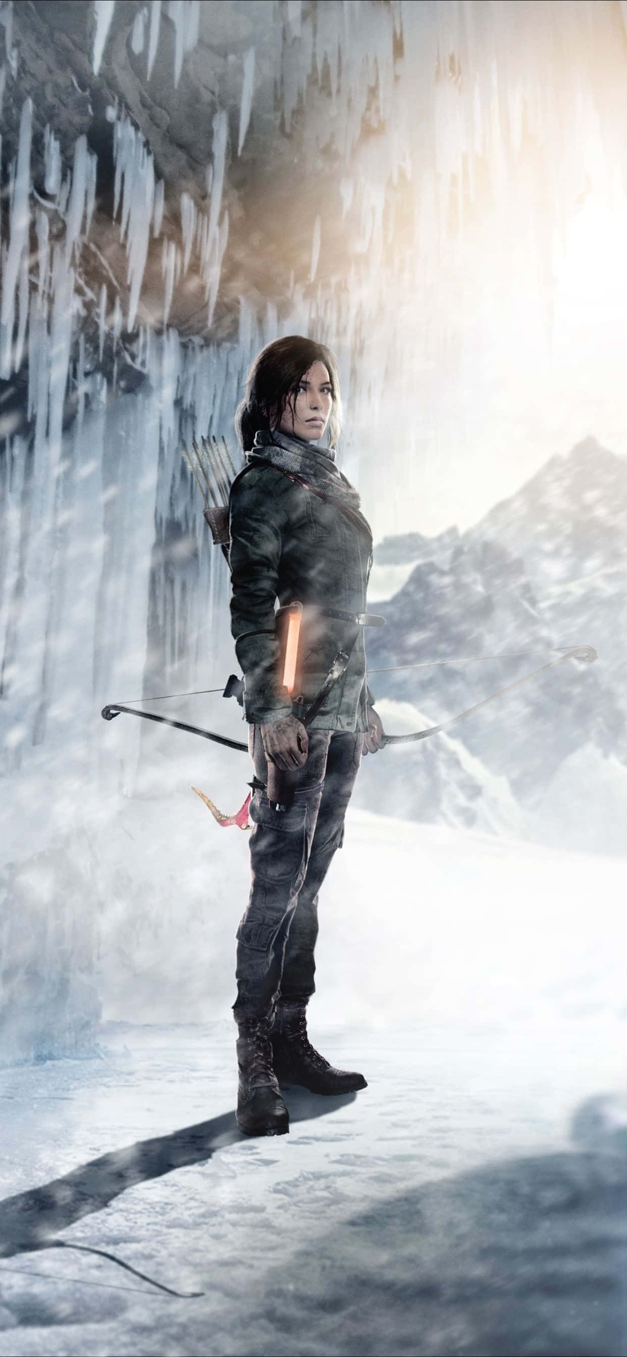 「在 iPhone Xs Max 上發掘《Rise of the Tomb Raider》的秘密與冒險」 壁紙 — 一位堅定的女弓箭手站在冰凍的山洞中，冰柱懸掛在她上方，背景是白雪覆蓋的山峰。