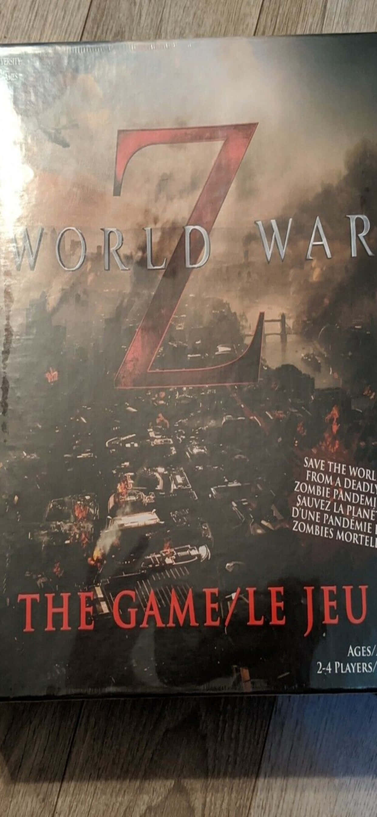 iPhone XS Max 屏幕上的《世界末日》黑暗影像 壁紙 — 《World War Z》的遊戲盒展示了一個混亂的殭屍末日場景，有燃燒的汽車和一個巨大的紅色Z標誌，背景是煙霧瀰漫的天空。