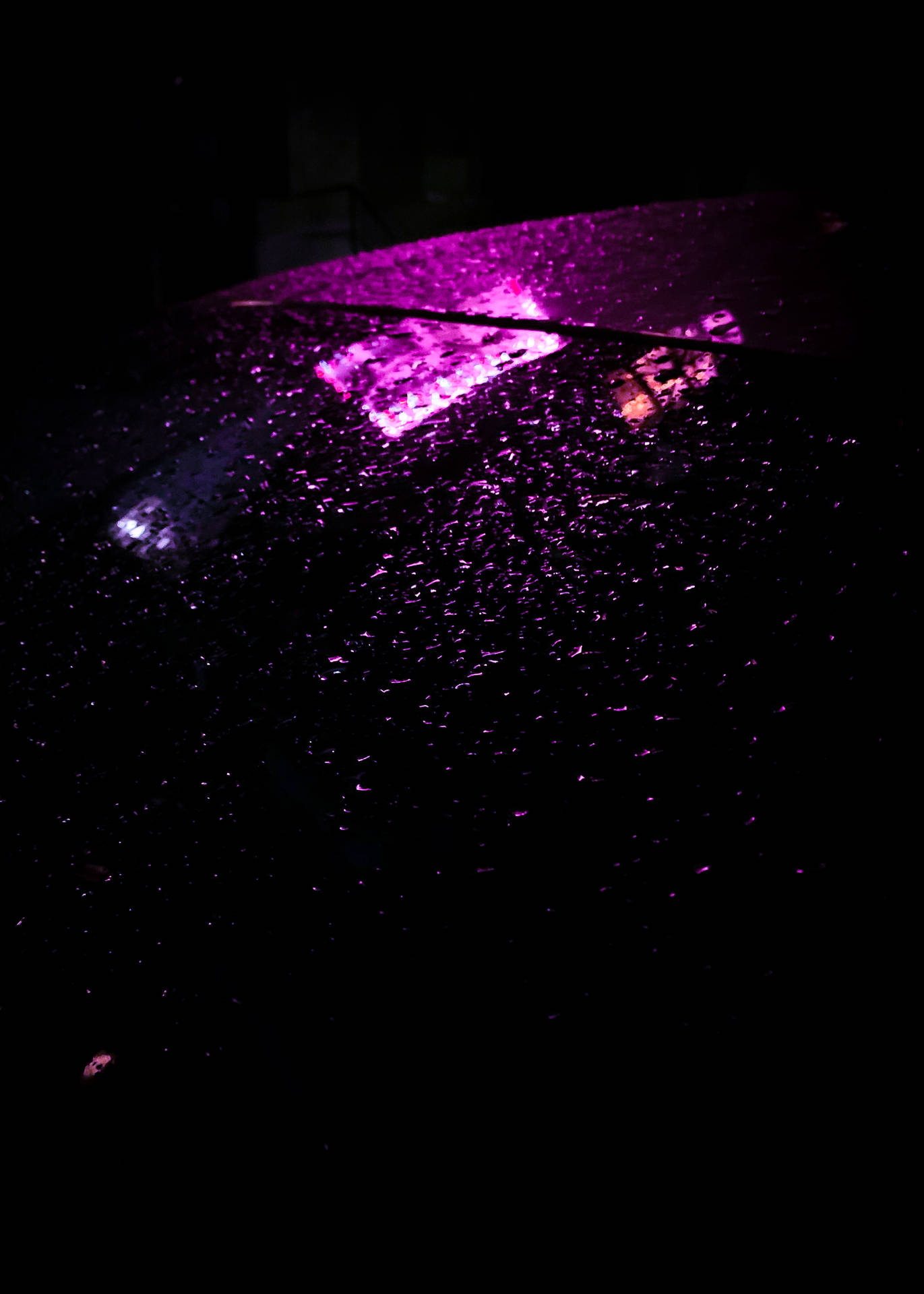 在漆黑的夜雨中，紫色霓虹燈反射在潮濕的汽車引擎蓋上。