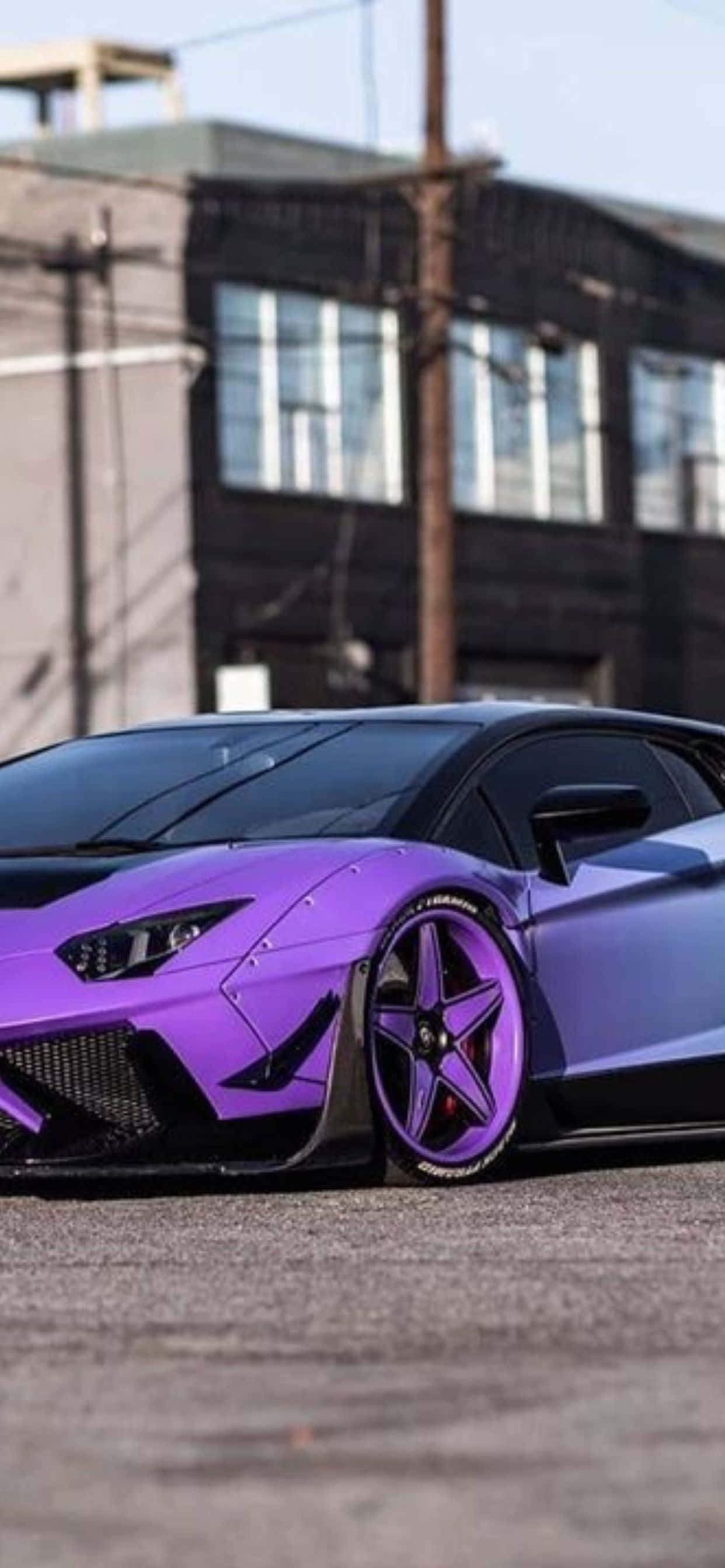 iPhone XS Max 紫黑蘭博基尼Aventador 背景 壁紙 — 一輛充滿活力的紫色林寶堅尼跑車停在瀝青路上，背景是工業建築。