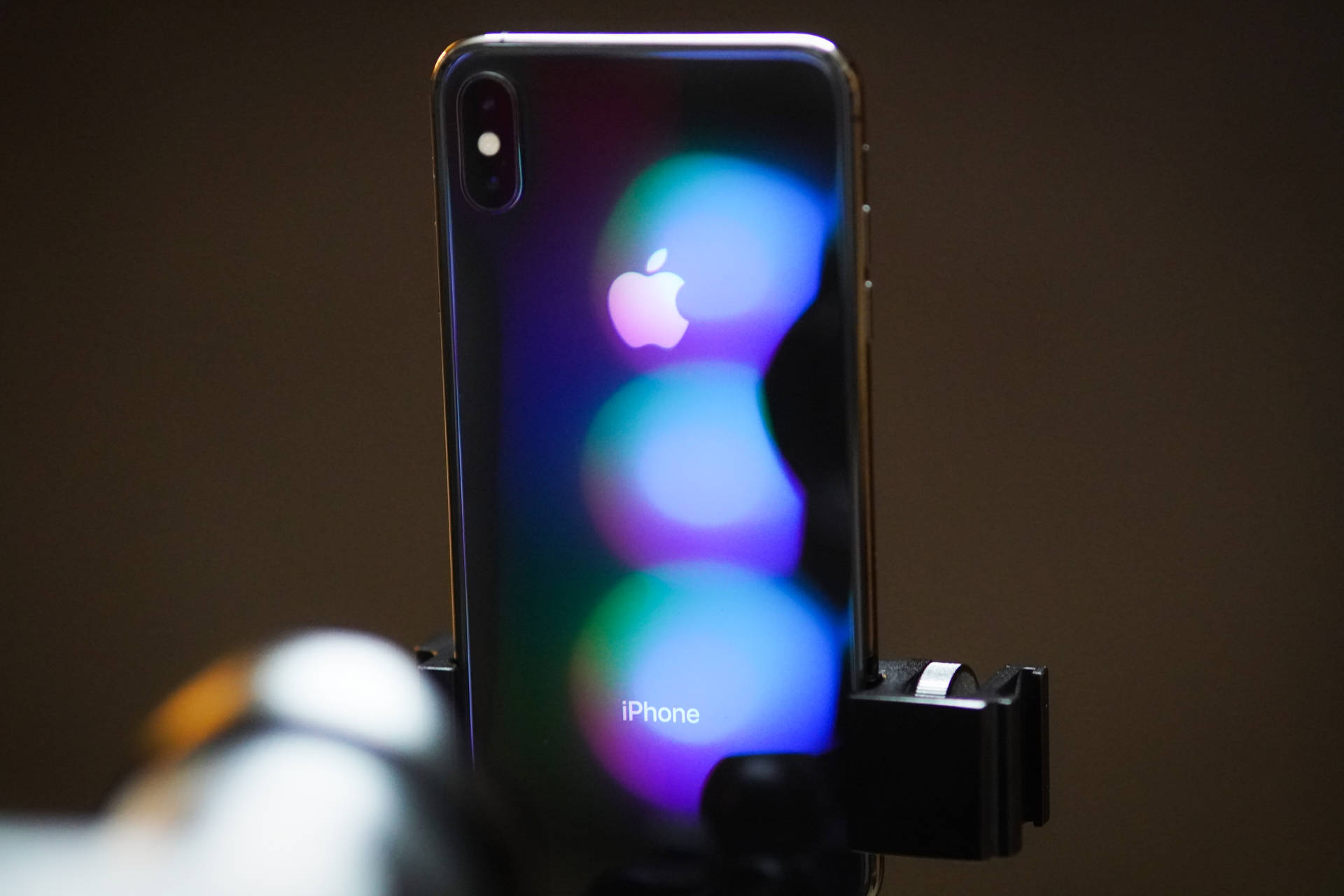 iPhone X 夾在夾具中，彩色模糊燈光反射在背面。