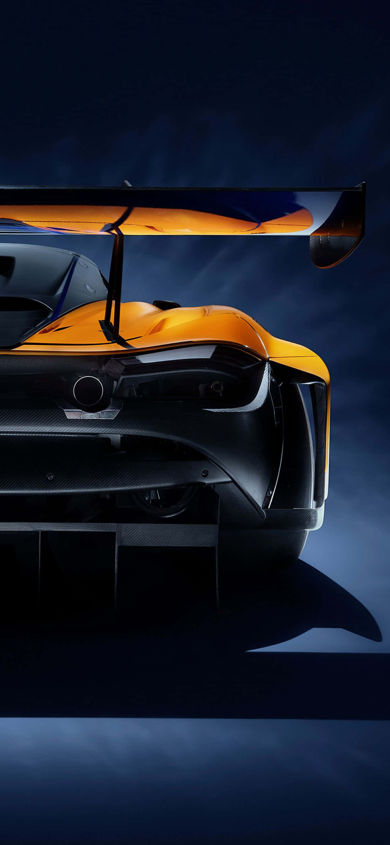 iPhone XS Max 與 McLaren 720S 跑車在震撼背景中並列 壁紙 — 一輛時尚的橙色和黑色跑車，帶有大型後擾流板，在深藍色工作室背景下戲劇性地照亮。