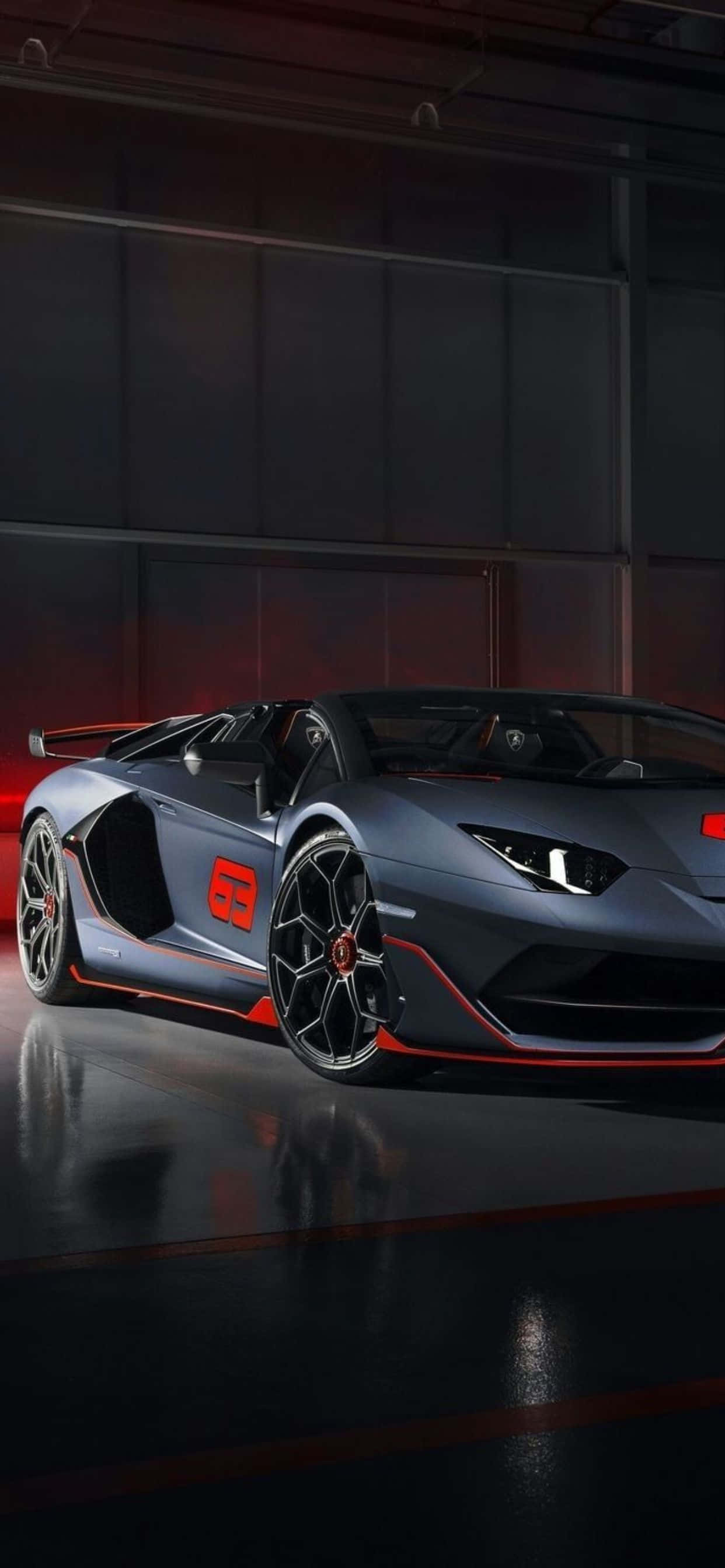 iPhone XS Max 蘭博基尼紅灰配色背景 壁紙 — 一架時尚的啞光灰色林寶堅尼Aventador，帶有鮮明的紅色點綴，在高科技車庫的戲劇性燈光下閃閃發光。