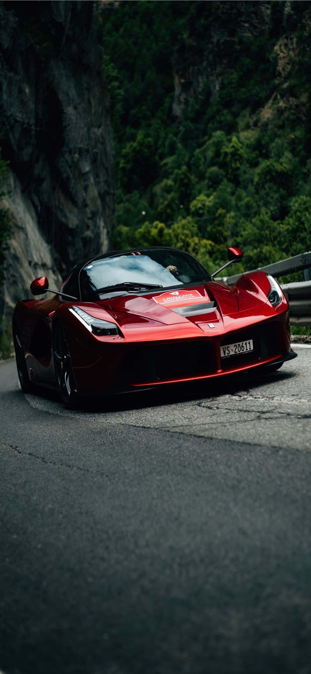 iPhone XS Max 賽車背景：亮紅色 LaFerrari 壁紙 — 一架光澤紅色法拉利LaFerrari跑車停泊在蜿蜒的山路上，周圍是茂密的綠色森林。