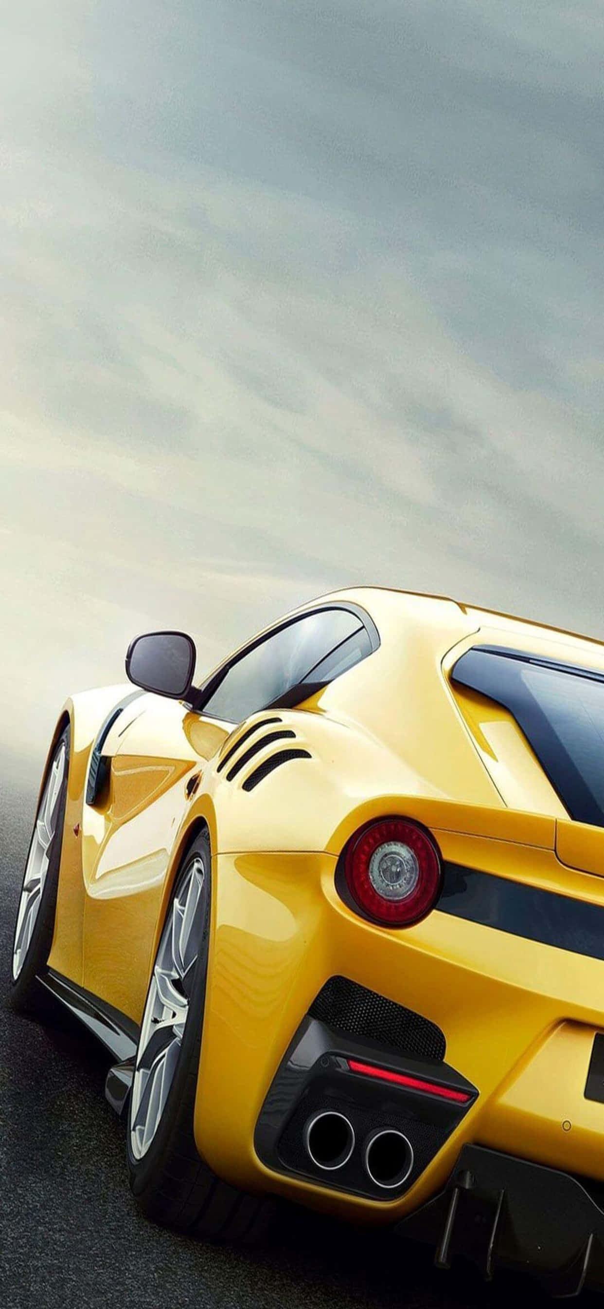 iPhone XS Max 賽車背景：黃色法拉利 F12tdf 壁紙 — 一輛充滿活力的黃色法拉利跑車向上傾斜，映襯著多雲的天空，擁有流暢的曲線和紅色尾燈。