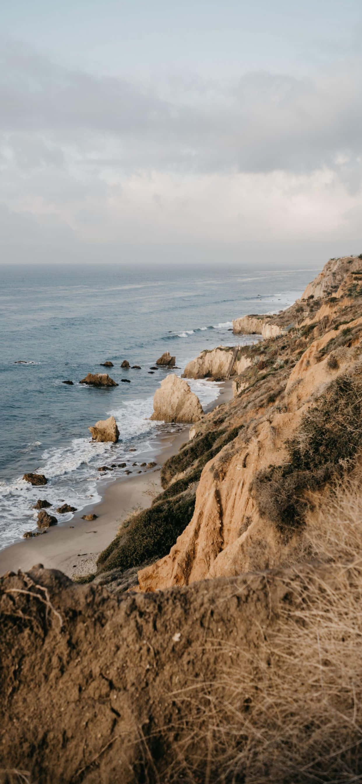 iPhone Xs Max 馬利布 El Matador 州立海灘背景 壁紙 — 寧靜的海岸懸崖，崎嶇的地形，俯瞰著柔和雲天下平靜的海洋。