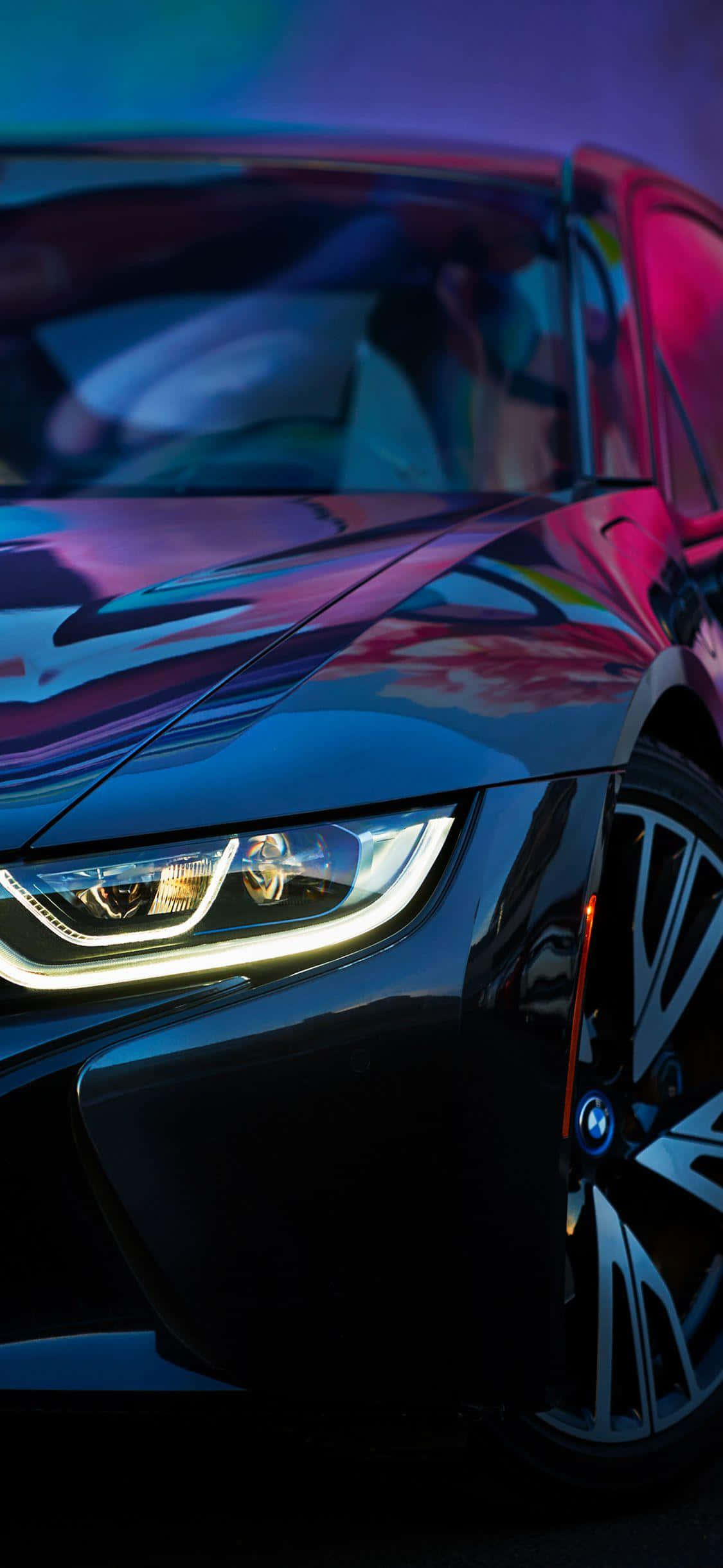 新款iPhone XS Max搭配《Project Cars 2》賽車遊戲 壁紙 — 一輛時尚的黑色跑車在霓虹燈下閃耀，光亮的表面反射出鮮豔的紫色和粉紅色光芒。