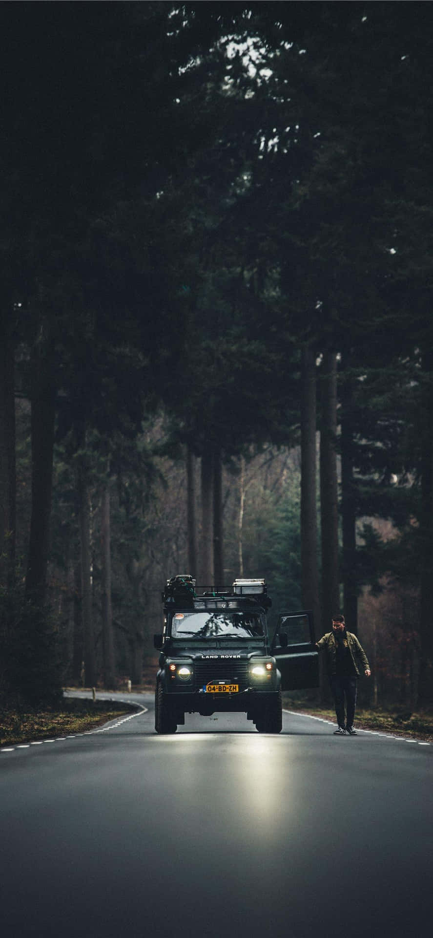 夜晚在森林道路上，一個人走在一輛停著的SUV旁邊。