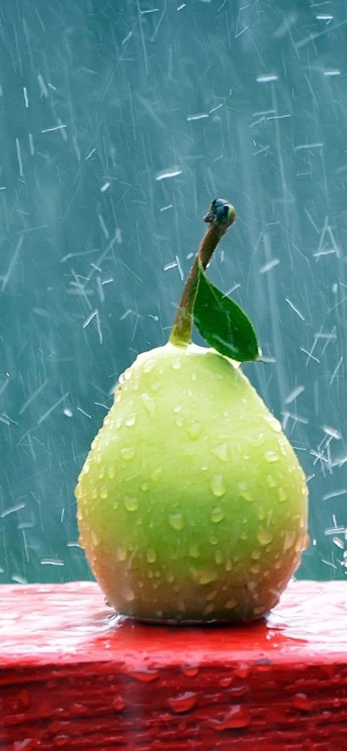 iPhone XS 桌面電腦青梨雨景背景 壁紙 — 一個帶有水珠的綠色梨子放在紅色表面上，背後有雨滴沿著青綠色窗戶流下。
