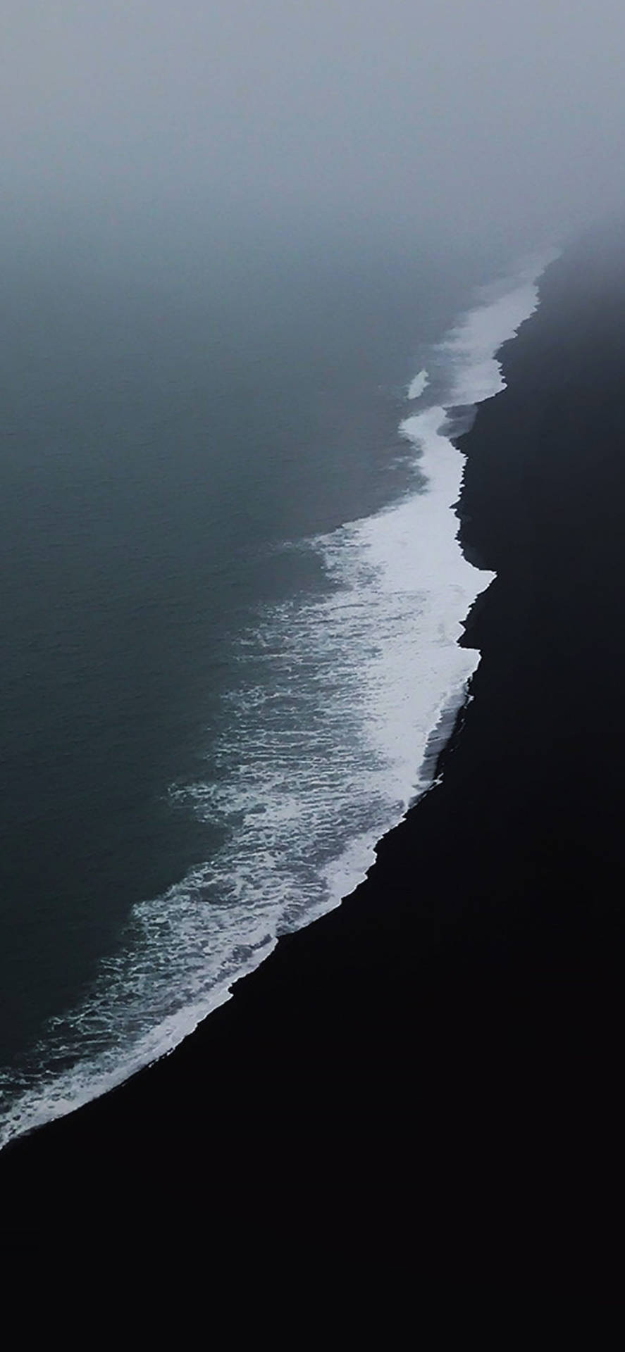 海浪在迷霧灰色天空下與黑色火山海岸相遇。