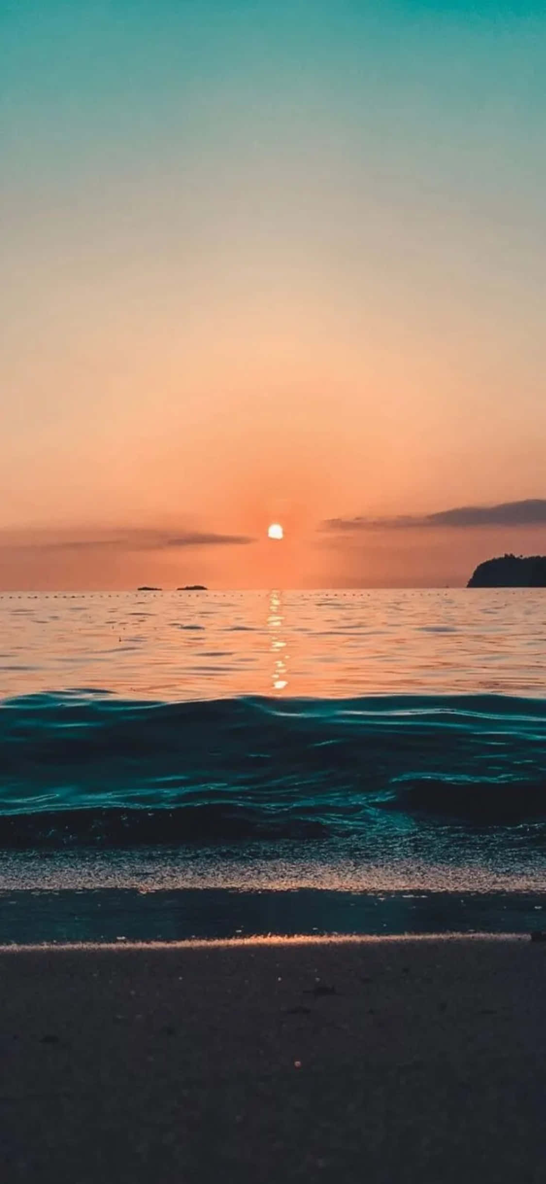 iPhone XS 海灘日落背景 壁紙 — 寧靜的日落，平靜的海面上，一輪發光的太陽在沙灘附近的水面上反射。