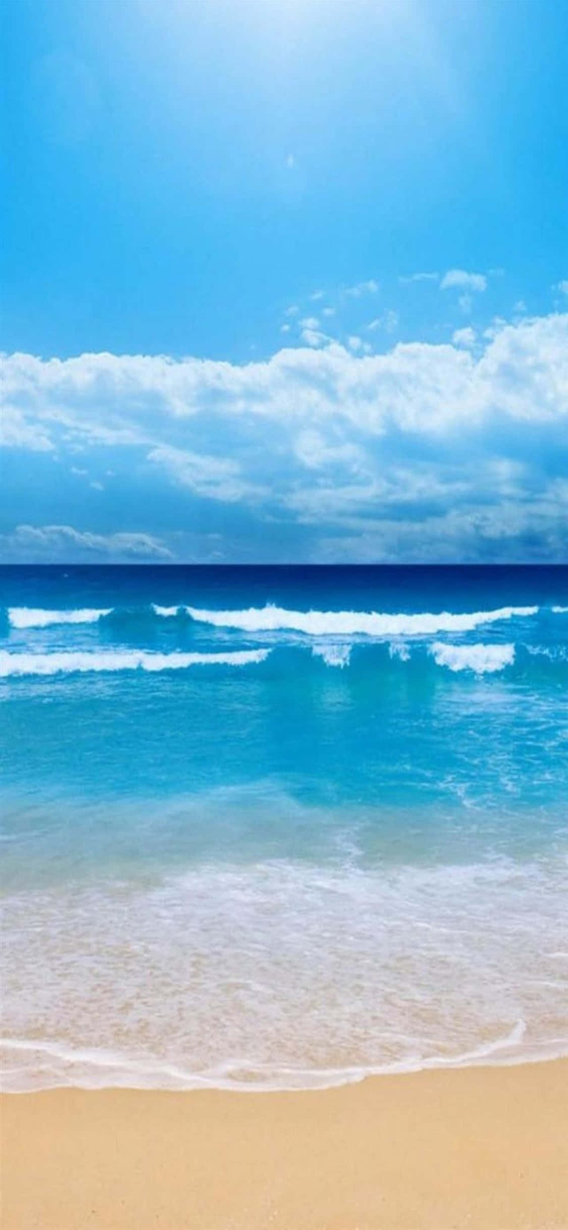 iPhone XS 海灘浪花拍岸背景 壁紙 — 陽光在碧綠色的海浪上閃爍，滾滾而來，拍打著金色的沙灘，頭頂是廣闊的藍天和蓬鬆的白雲。