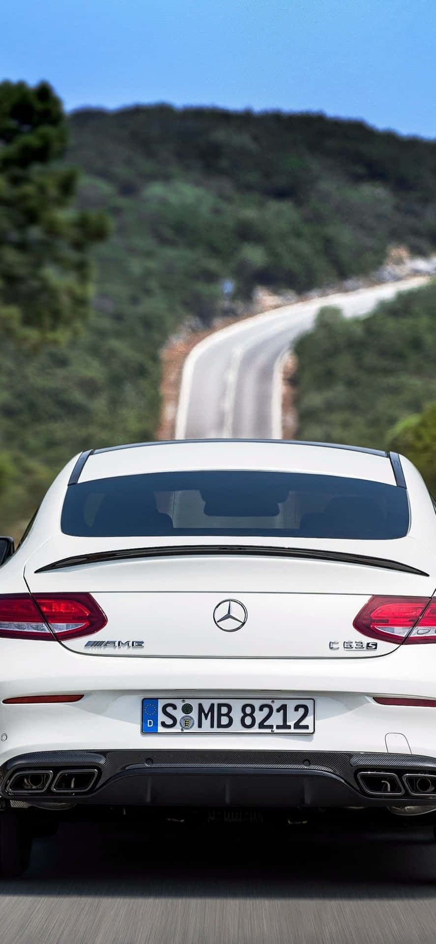 白色平治AMG C63 S在日落時分行駛於蜿蜒山路。