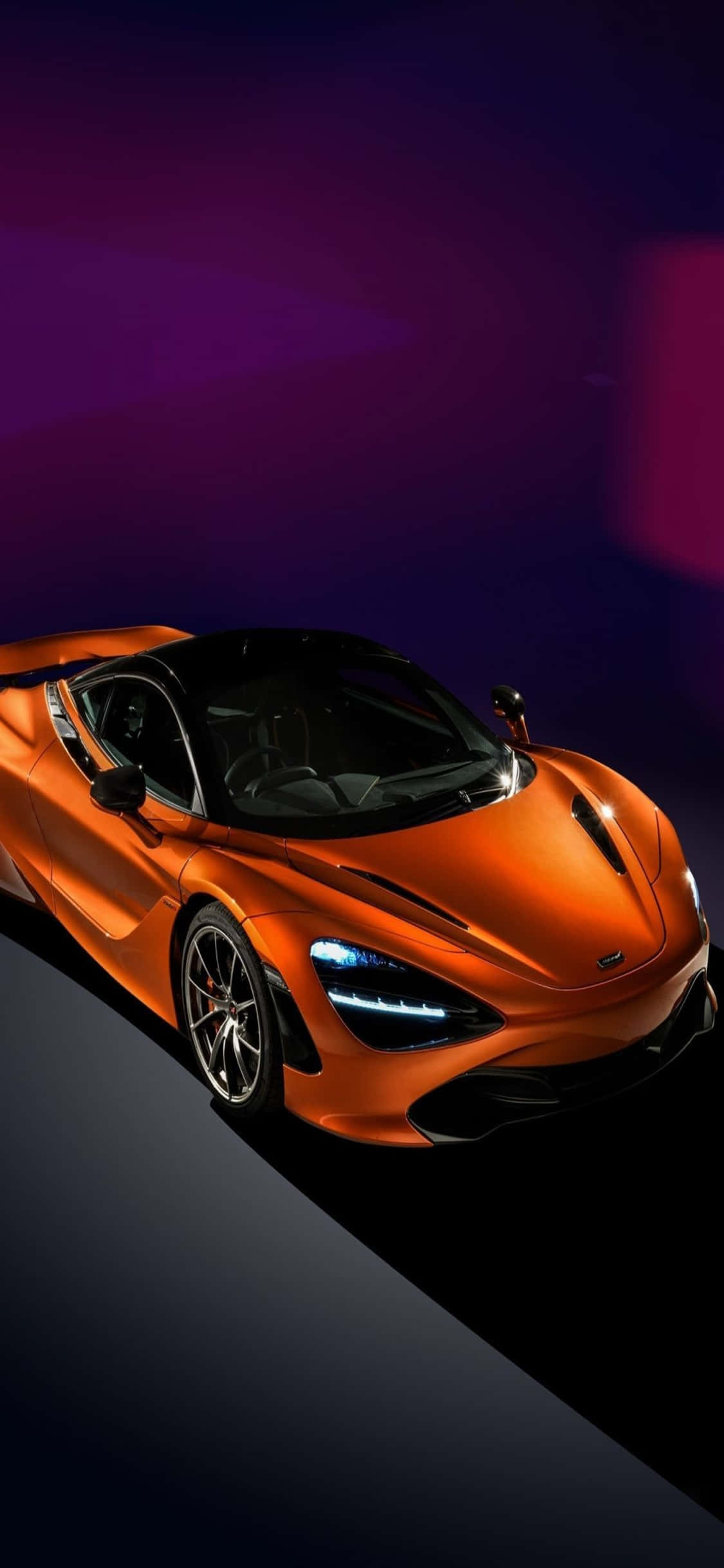 iPhone Xs 與 McLaren 720s 的極致組合 壁紙 — 一輛時尚的橙色跑車在黑暗的攝影棚背景下，在戲劇性的紫色燈光下閃耀。