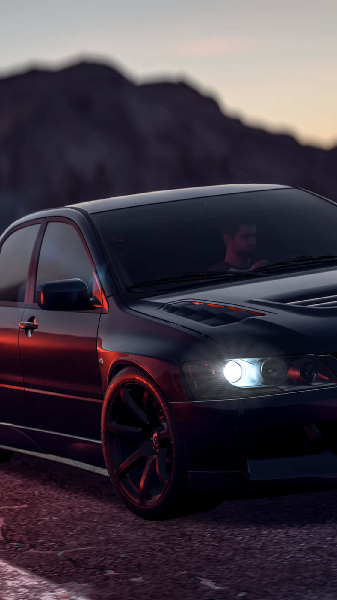 iPhone XS《Need For Speed Payback》深色三菱Lancer Evolution壁紙 壁紙 — 一輛時尚的黑色跑車，帶有發光的車頭燈，停泊在黃昏的碎石路上，背景是山脈。