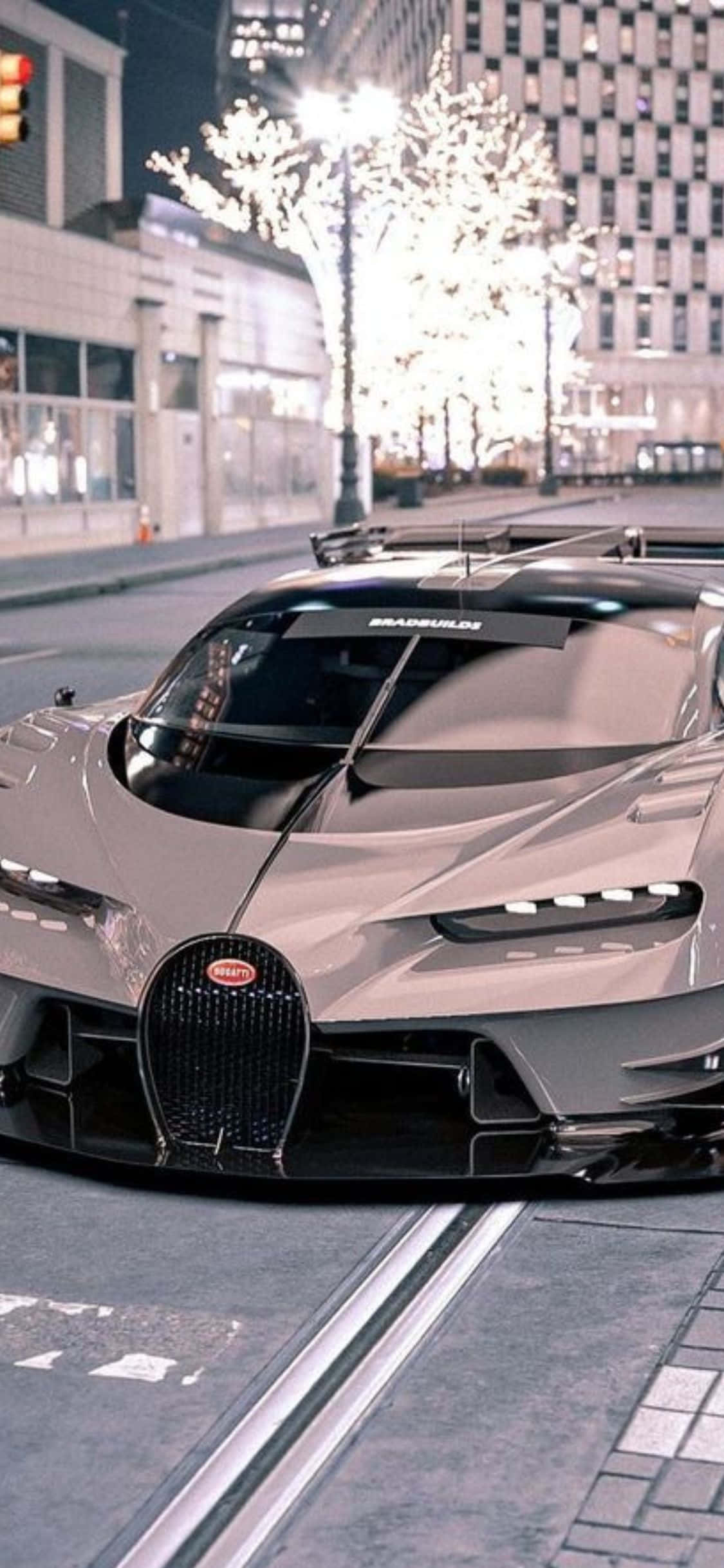 iPhone XS與Bugatti的風格與速度無可匹敵 壁紙 — 一輛時尚的銀色 Bugatti 超跑停在夜晚的城市街道上，背景是燈光璀璨的樹木和現代建築。