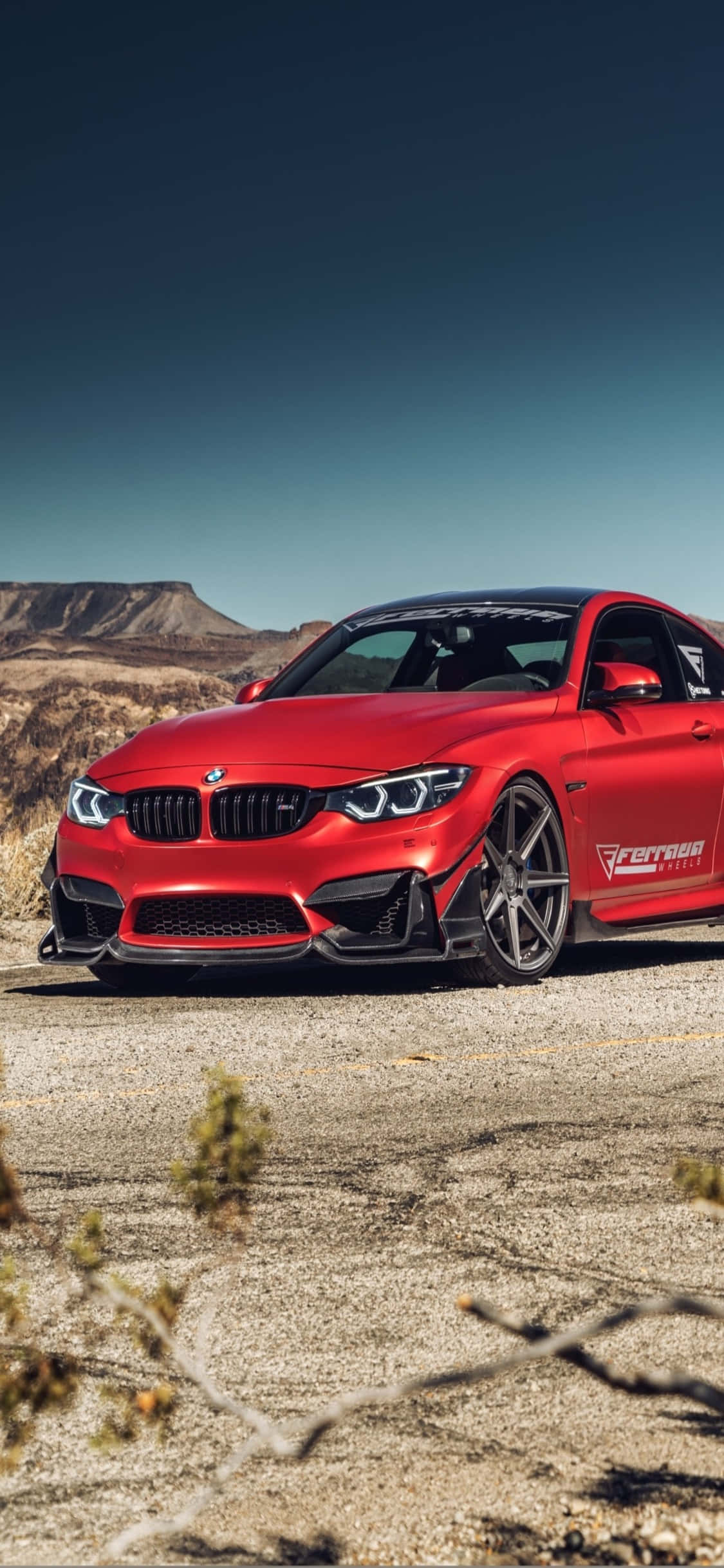 iPhone X與BMW的奢華體驗 壁紙 — 一輛鮮紅色BMW M4雙門轎跑車，帶黑色飾件，停泊在龜裂的沙漠地面上，天空湛藍清澈。