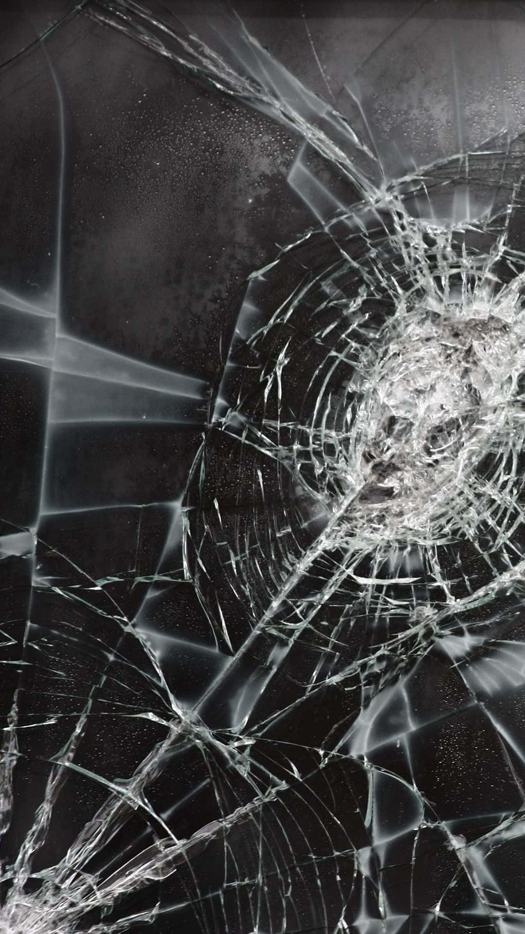 iPhone 屏幕裂縫惡作劇照片 壁紙 — 一塊破碎的玻璃表面，從中央撞擊點向外輻射出複雜的裂紋，背景為深色。