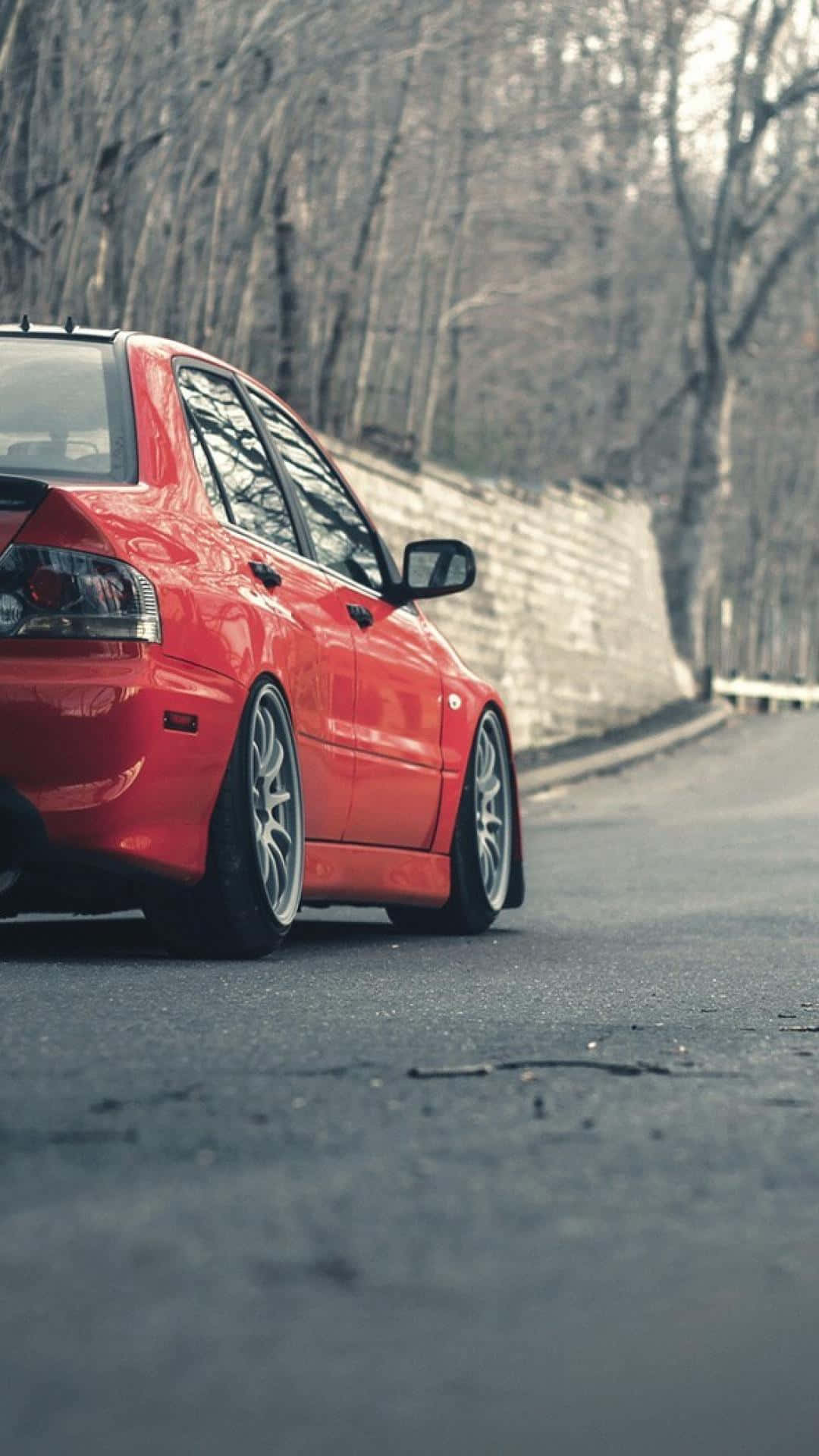 紅色跑車停泊在彎曲的道路旁，旁邊有石牆和光禿禿的樹木。