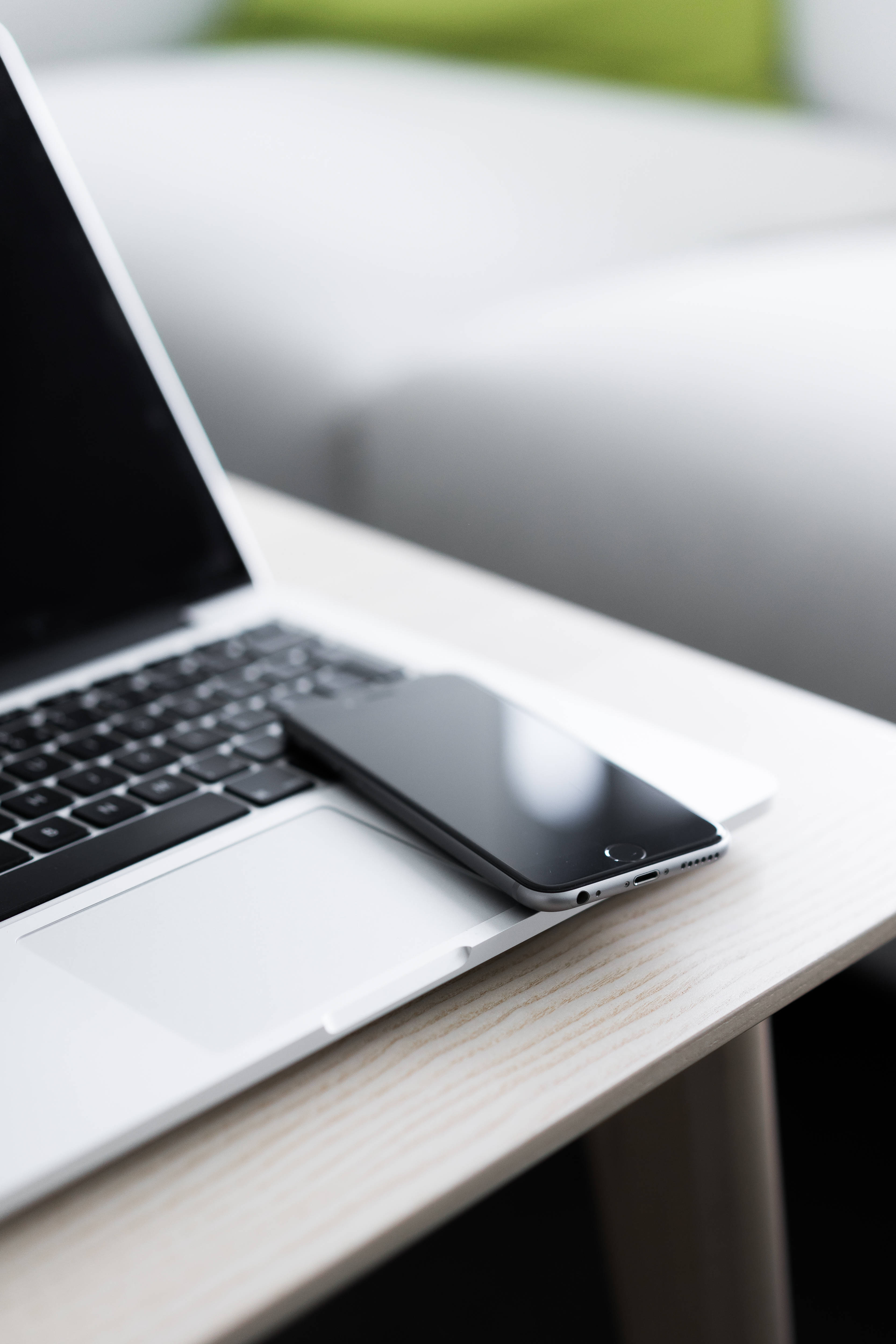 iPhone 放在 MacBook Air 2020 上 壁紙 — 一部時尚的銀色手提電腦和黑色智能手機放在淺色木桌上，旁邊是模糊的白色梳化。