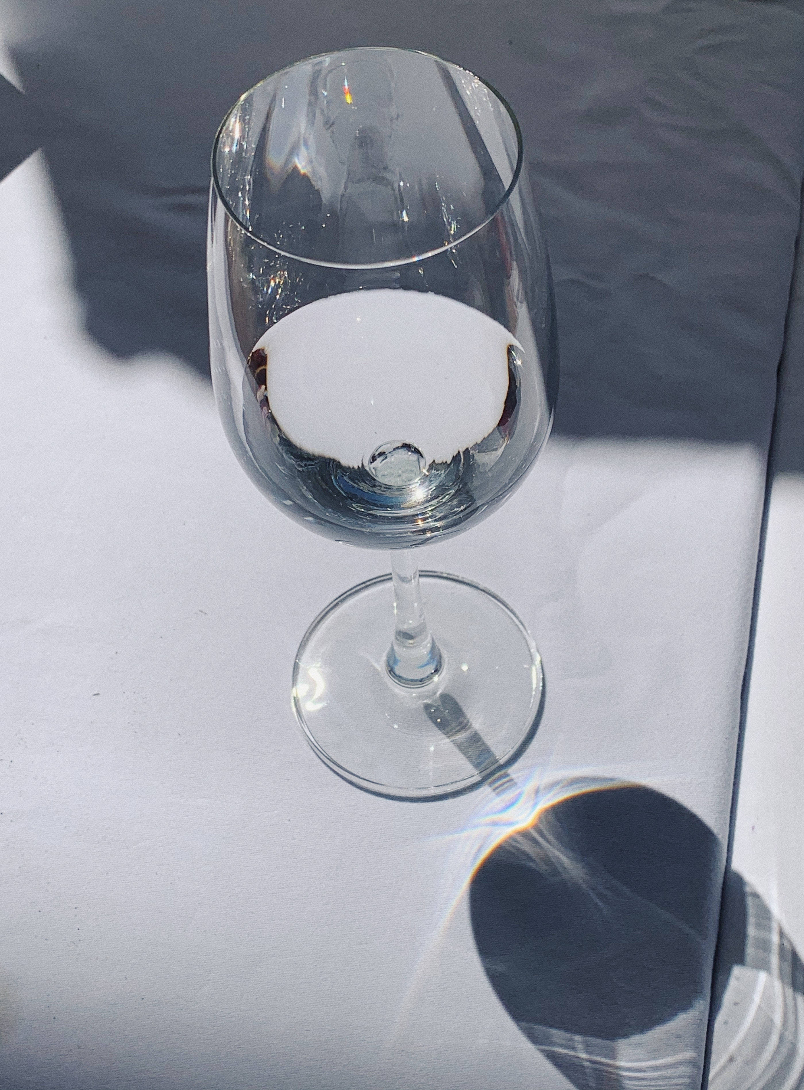 iPhone 水杯鎖屏壁紙 壁紙 — 一個透明酒杯立在白色表面上，在明亮的陽光下投下清晰的陰影。