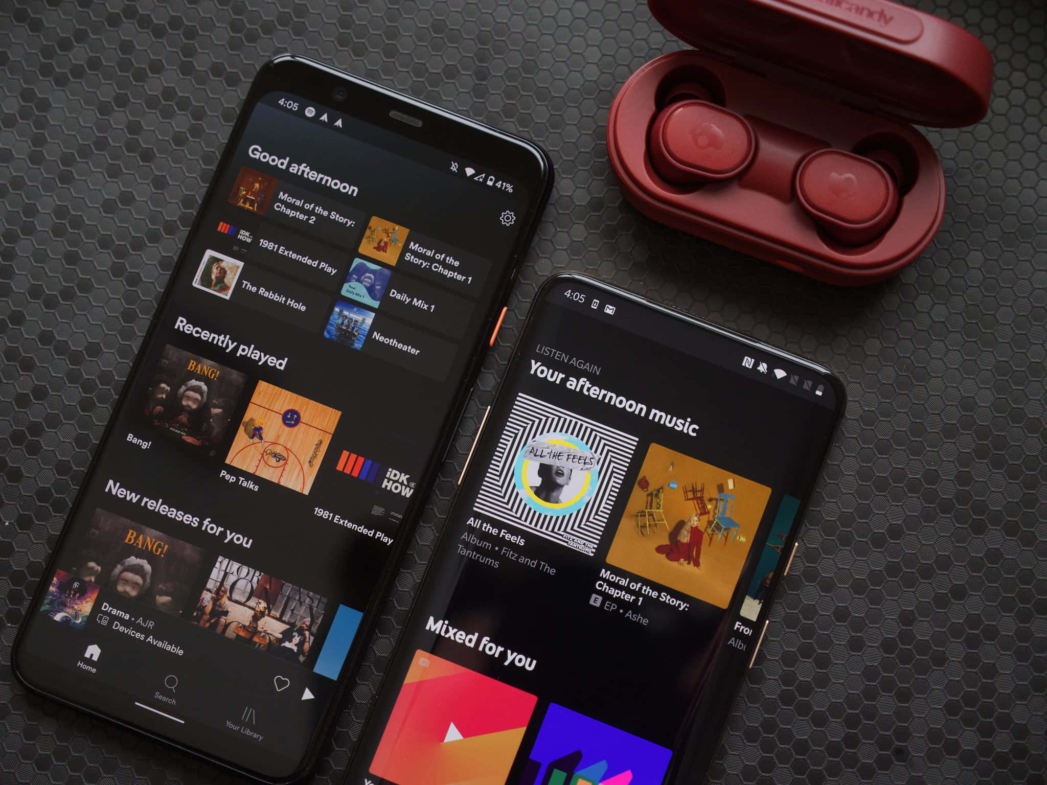 iPhone 與 Android 歌曲圖片 壁紙 — 兩部顯示音樂應用程式的智能手機放在紅色無線耳機旁邊，置於深色六角形紋理表面上。