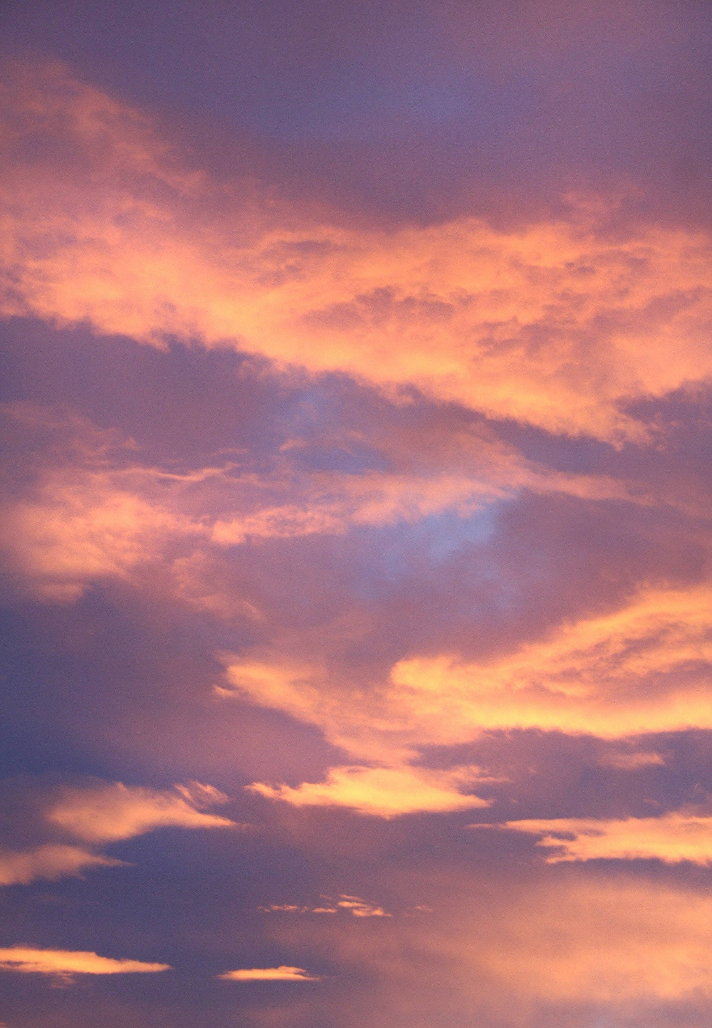 iPhone 解鎖畫面 夕陽天空 壁紙 — 日落時分，火橙色和柔紫色雲彩在地平線上翻騰的戲劇性天空。