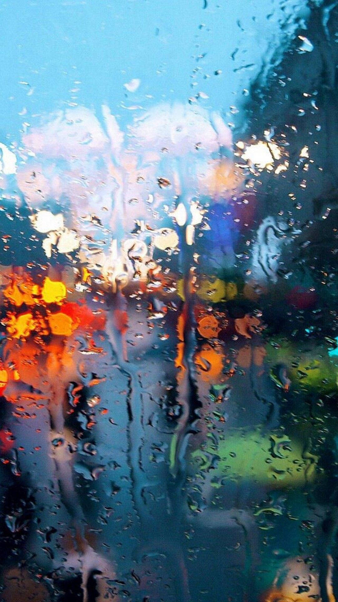雨點在夜間扭曲玻璃窗上色彩繽紛的城市燈光。