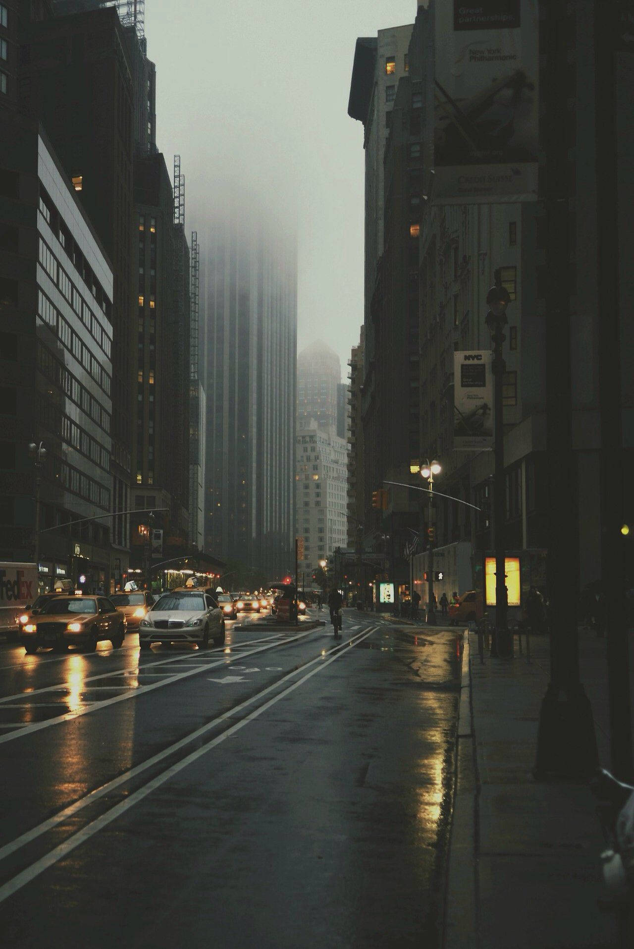 黃昏時分的雨街，濕漉漉的路面和霧中的摩天大樓。