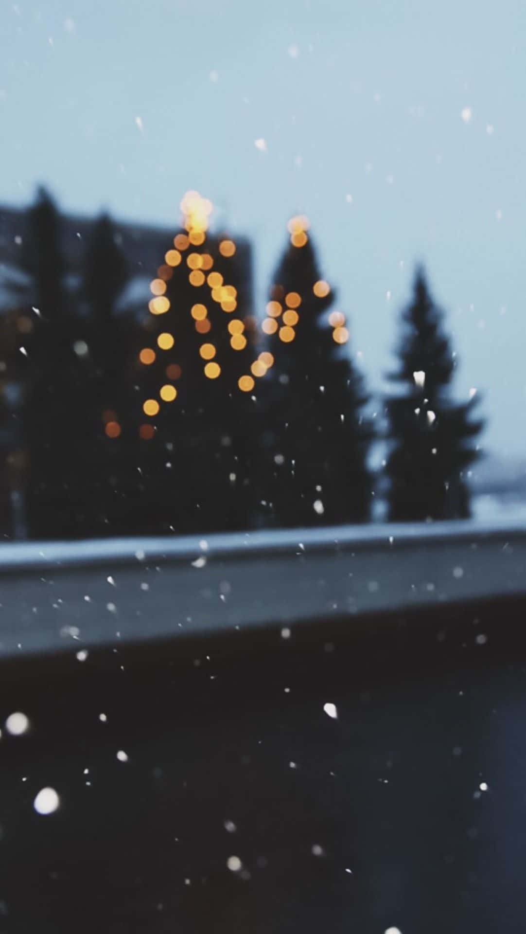 iPhone聖誕節美學雪景濾鏡 壁紙 — 雪花飄過車窗，模糊的金色燈光在暮色天空中形成節日樹的剪影。