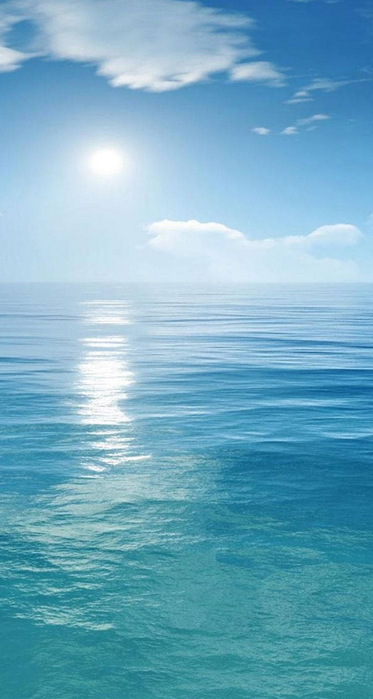 陽光在平靜的海面上反射，天空湛藍，有雲朵。