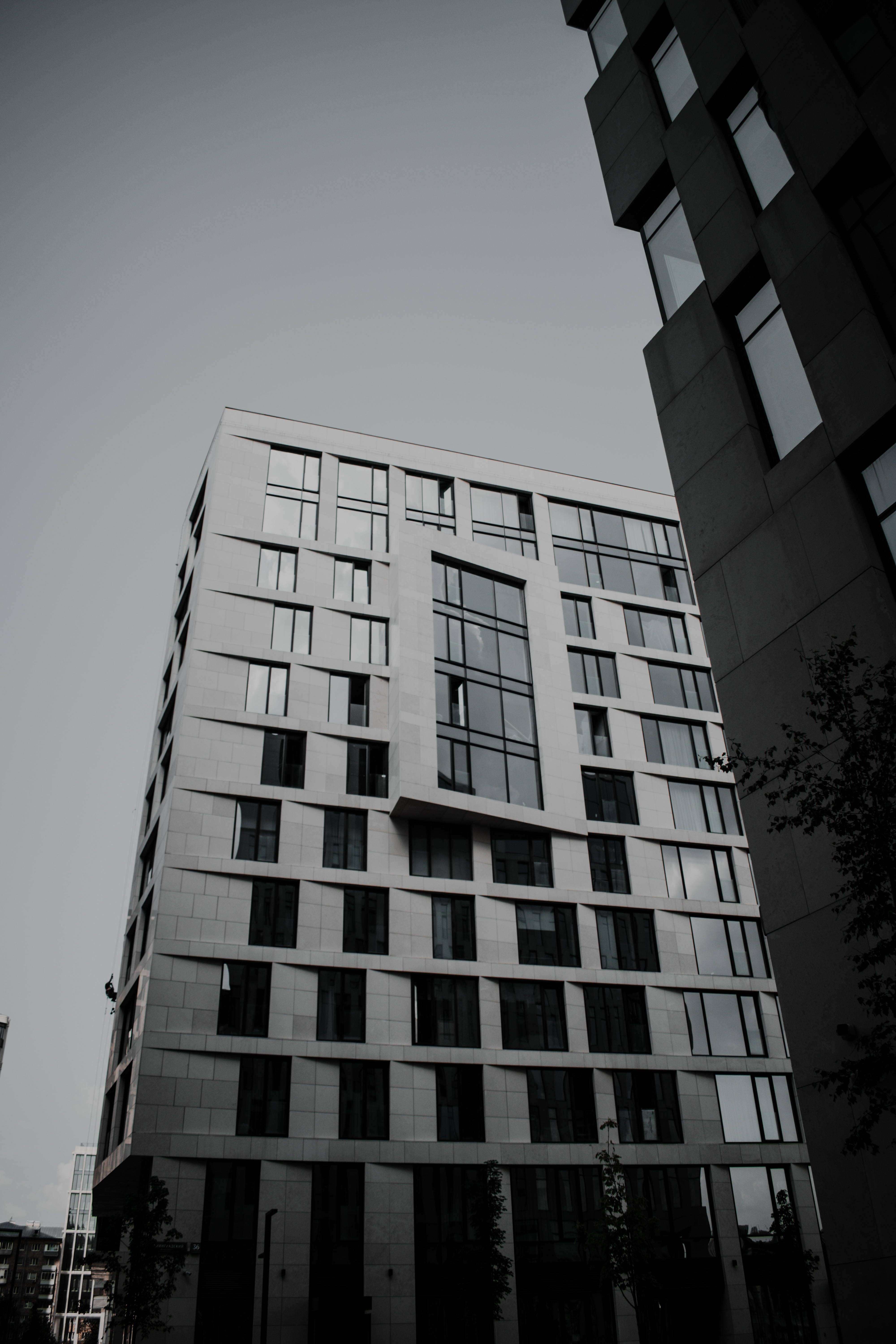iPhone黑白建築外牆攝影 壁紙 — 一張低角度黑白照片，拍攝了一座現代玻璃和鋼結構公寓大樓，聳立在柔和的天空下。