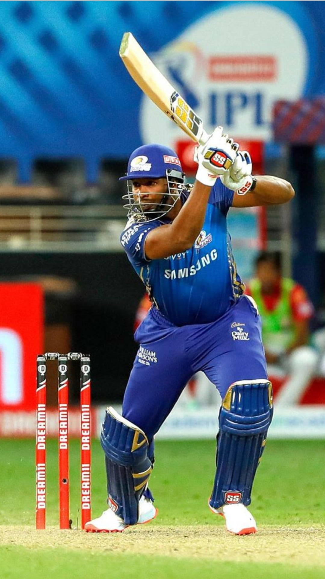 IPL 2021 庫倫·波拉德賽場風采 壁紙 — 身穿藍色球衣的板球手在明亮的燈光下於球場強力揮棒。