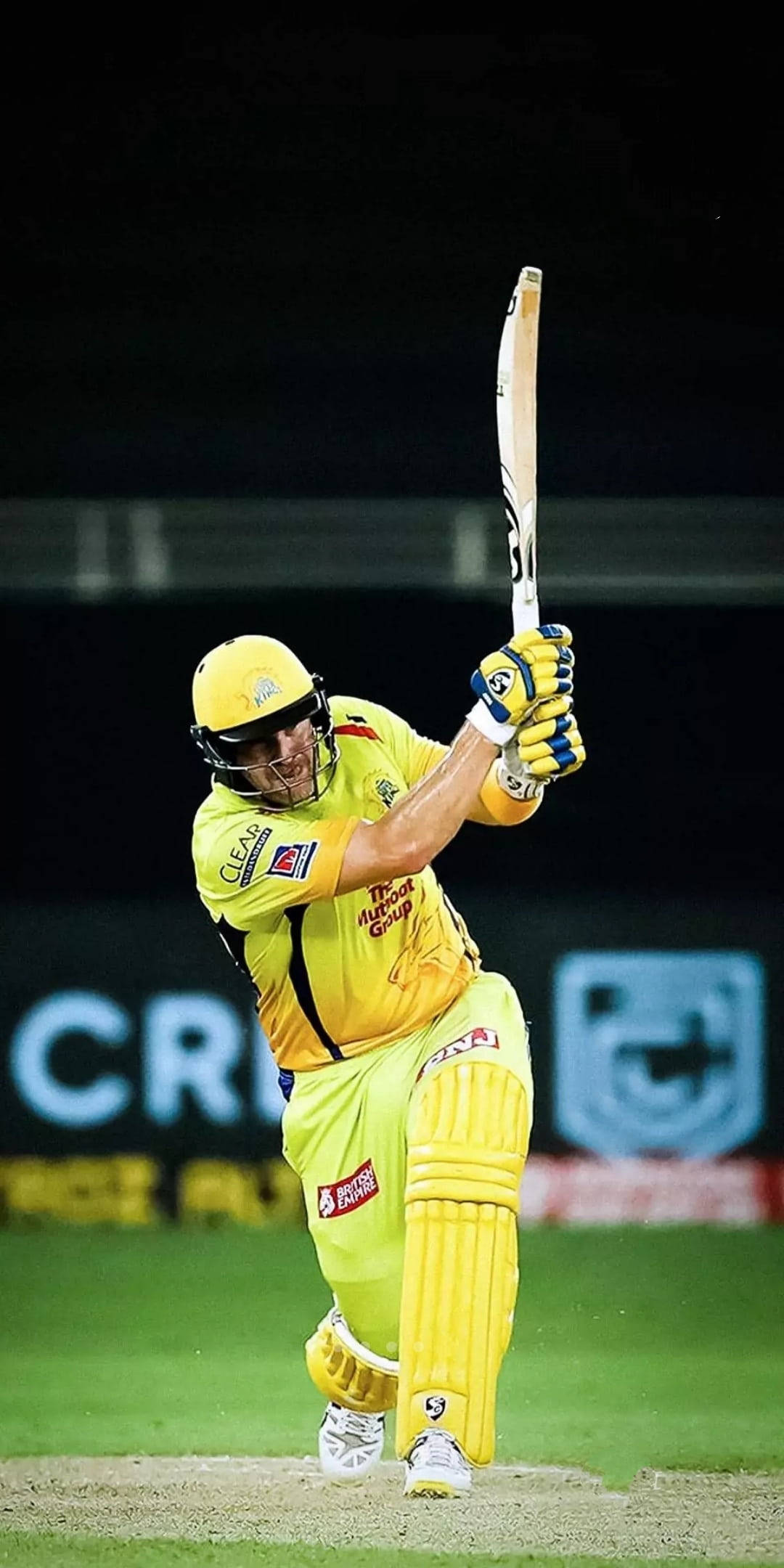 IPL 2021 謝恩·沃森身穿黃色戰袍 壁紙 — 一名身穿亮黃色裝備的板球擊球手在夜間球場燈光下強力揮棒。