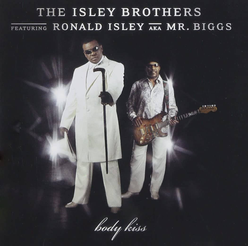 Isley Brothers 與 Ronald Isley《Body Kiss》專輯造型 壁紙 — 兩位穿著白色西裝的時尚黑人男性在黑暗背景下自信地擺姿勢，身後有明亮的舞台燈光閃耀。