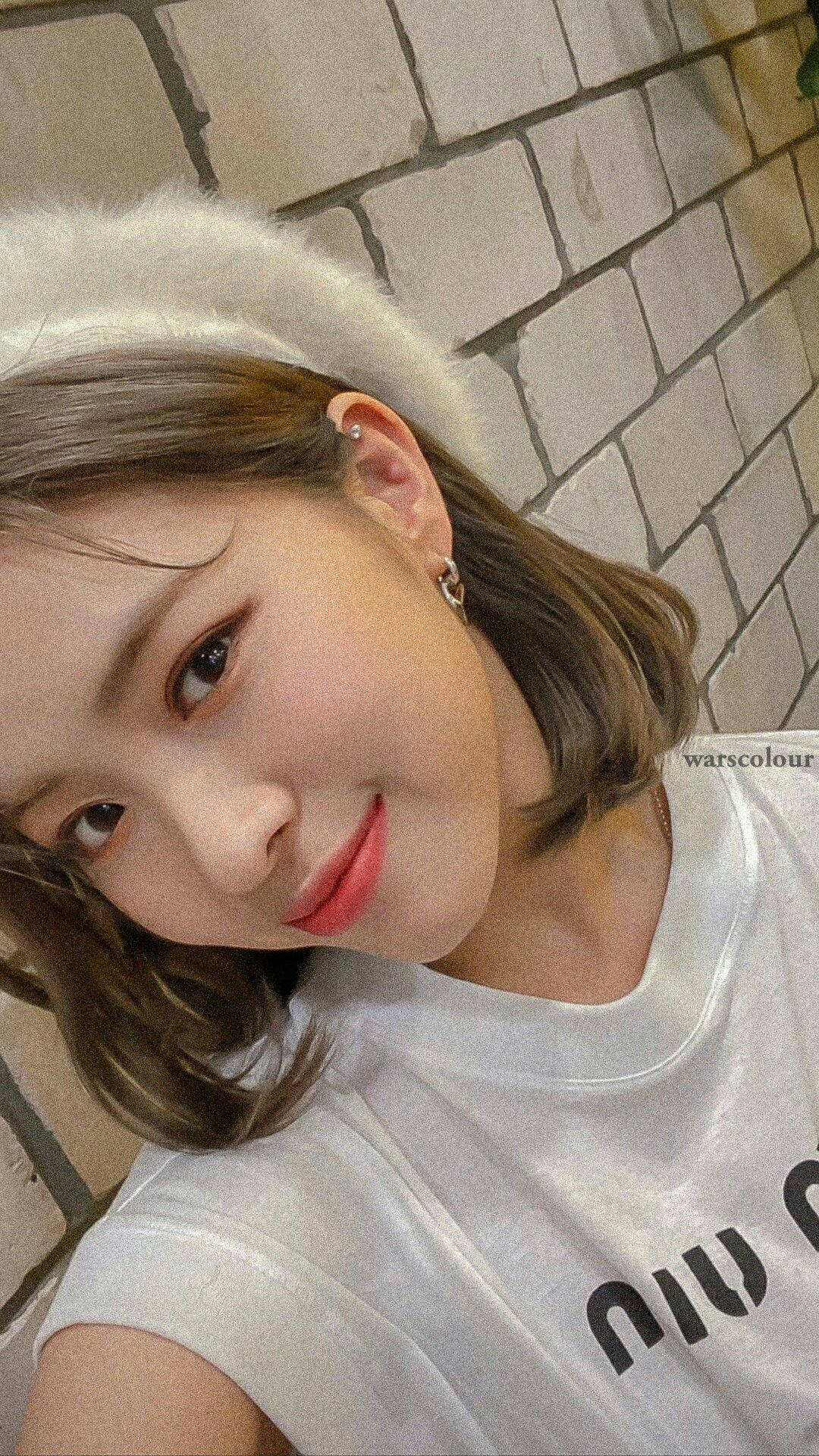 ITZY 中心申留真 壁紙 — 一位短棕髮、戴白色毛絨頭帶的年輕女性，在淺色磚牆背景下溫柔微笑。