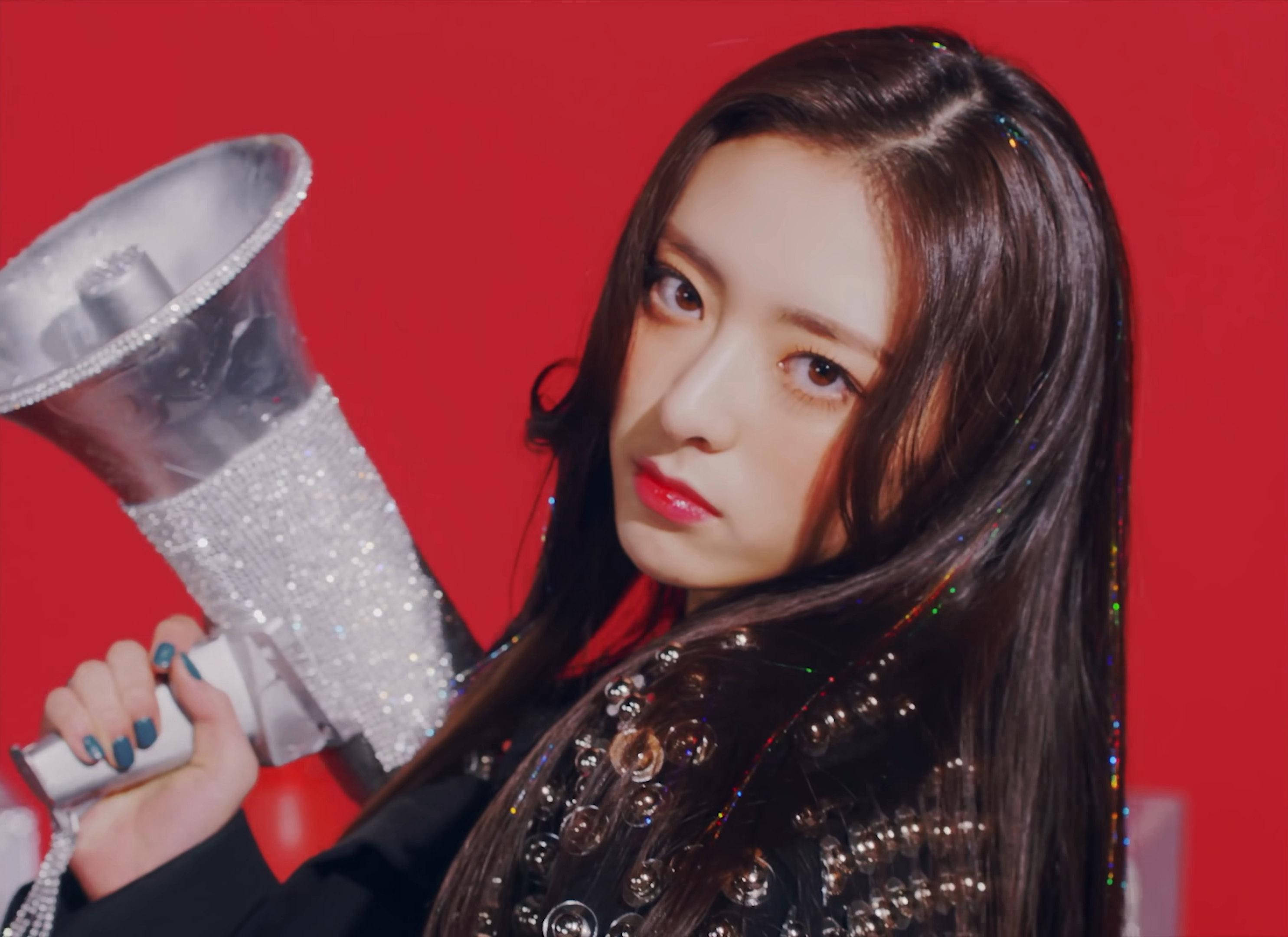 ITZY 忙內申有娜 壁紙 — 一位長黑髮的年輕女性在鮮紅色背景前拿著閃閃發光的擴音器。