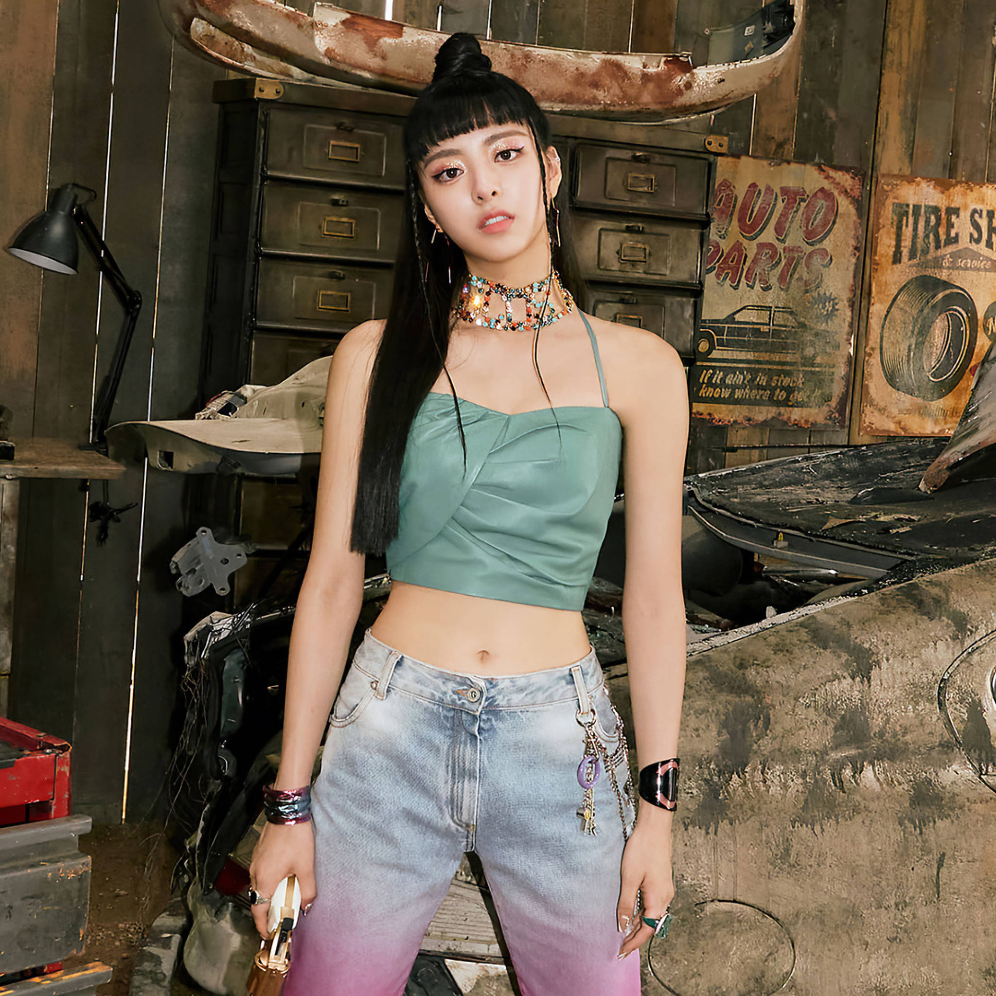 ITZY 申有娜《Not Shy》 壁紙 — 一位年輕女性身穿綠色短版上衣和漸變牛仔褲，在充滿復古標誌和工具的鄉村風格汽車修理廠自信地擺姿勢。
