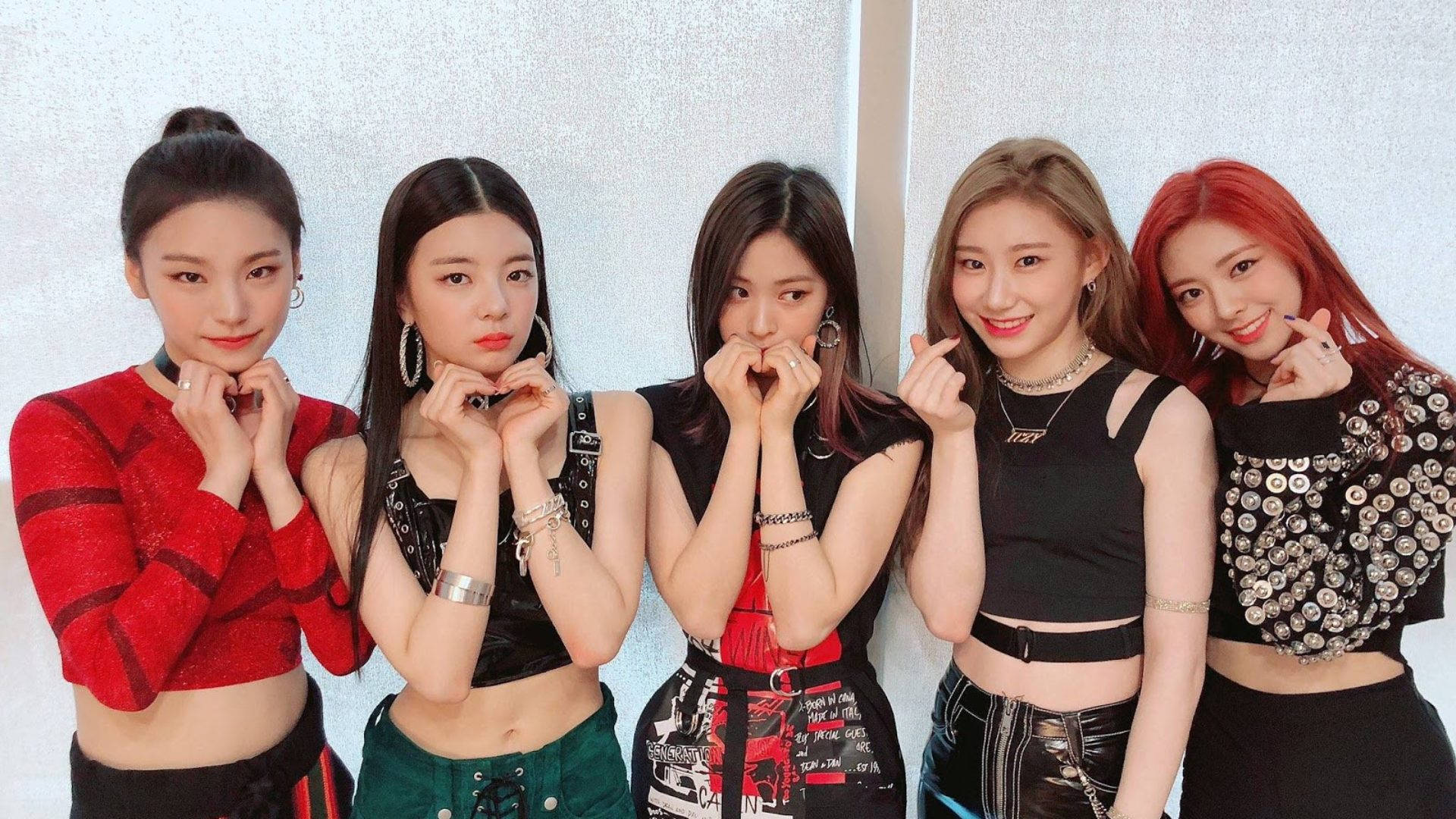 ITZY 首演舞台照 壁紙 — 五位時尚年輕女性穿著潮流服裝，在帶有紋理的白色牆壁前自信地擺出俏皮的手勢。